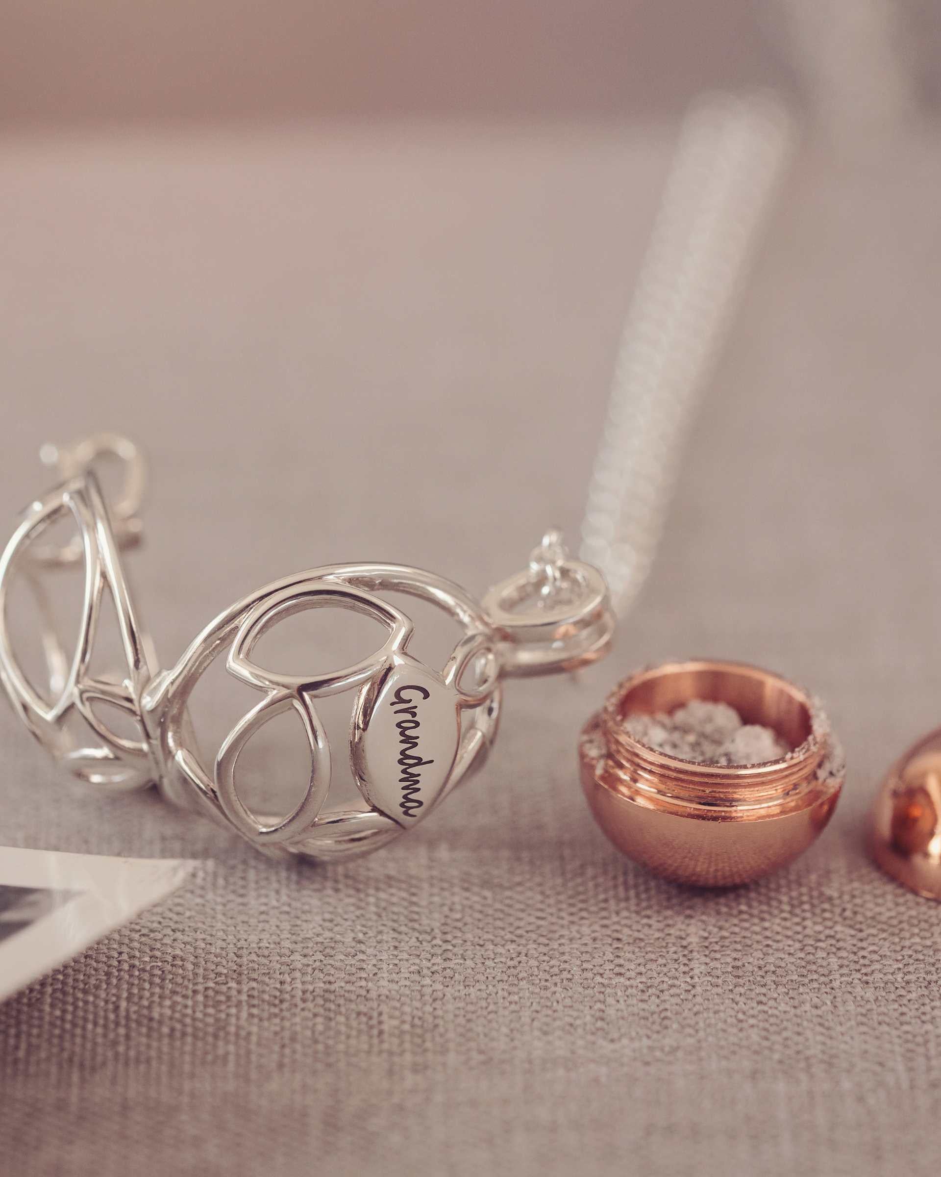 Silver necklace with 'Grandma' pendant and ash urn on a textured surface