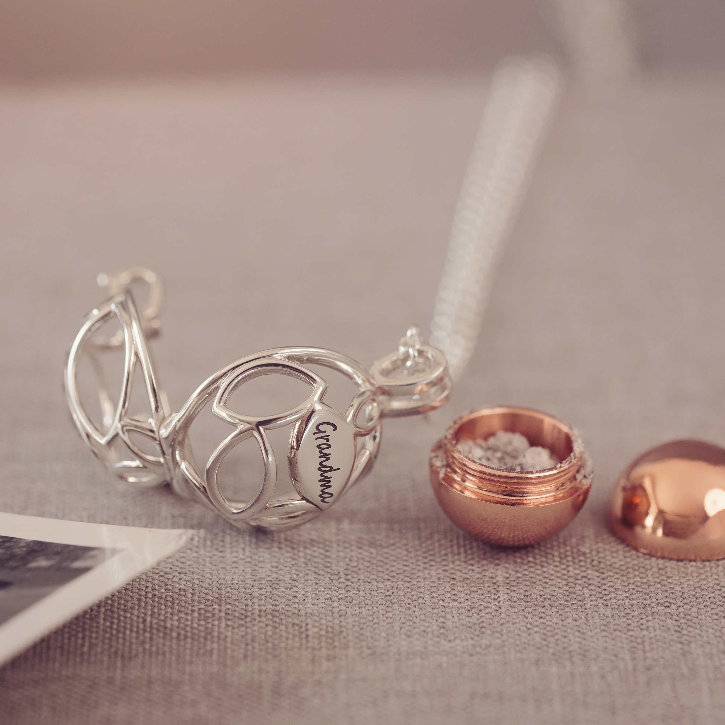 Silver necklace with 'Grandma' pendant and ash urn on a textured surface
