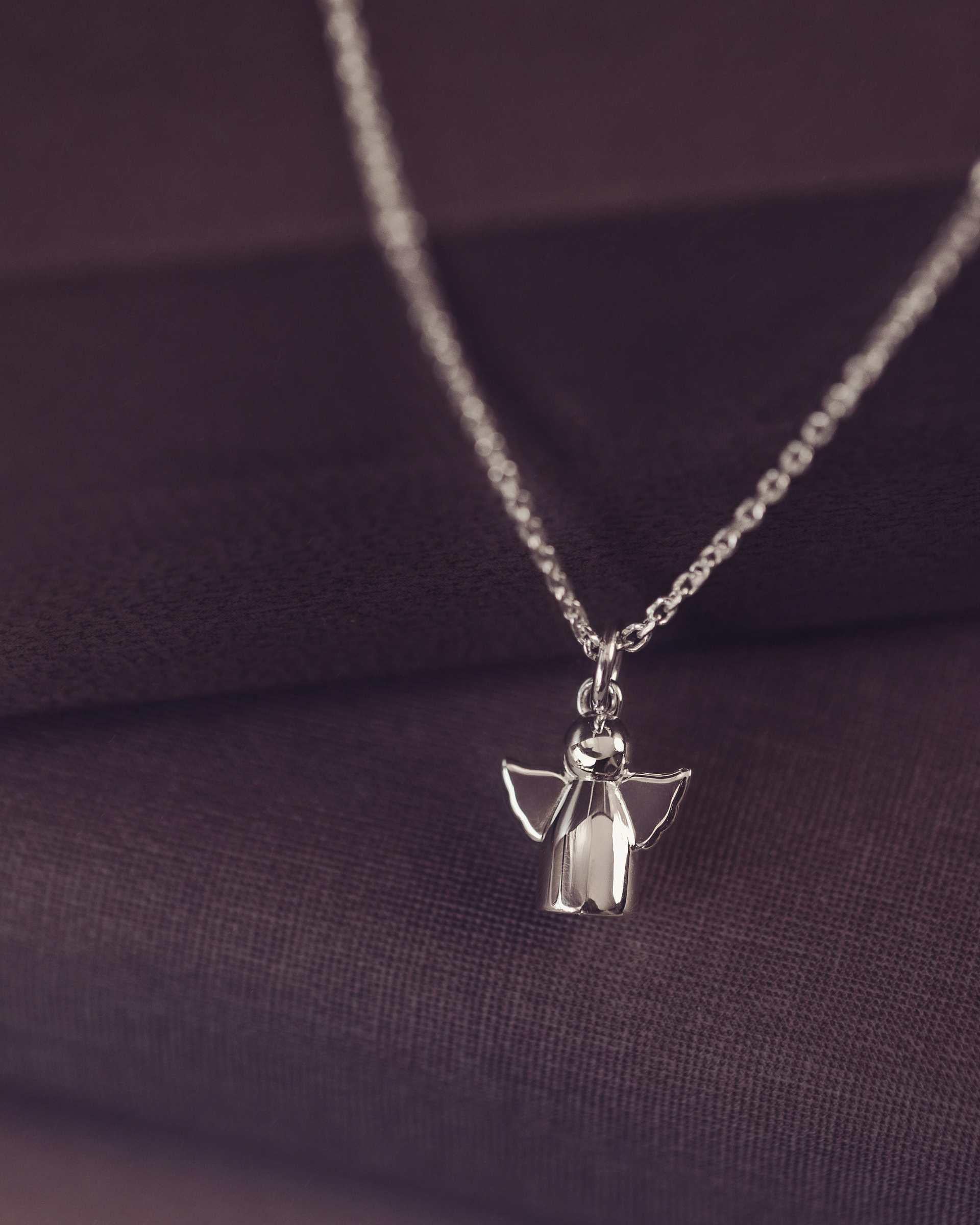 Silver angel pendant necklace on a dark fabric background