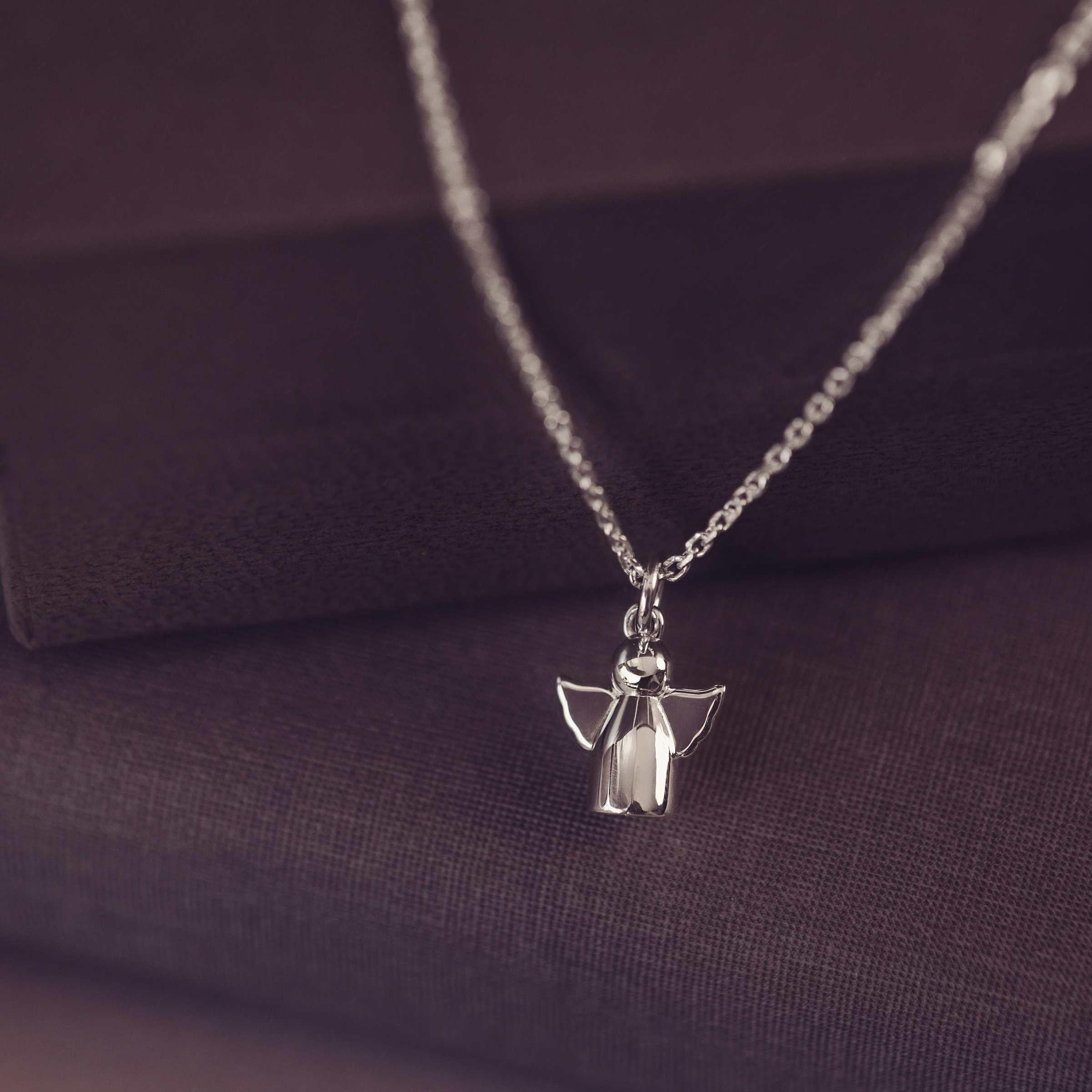 Silver angel pendant necklace on a dark fabric background