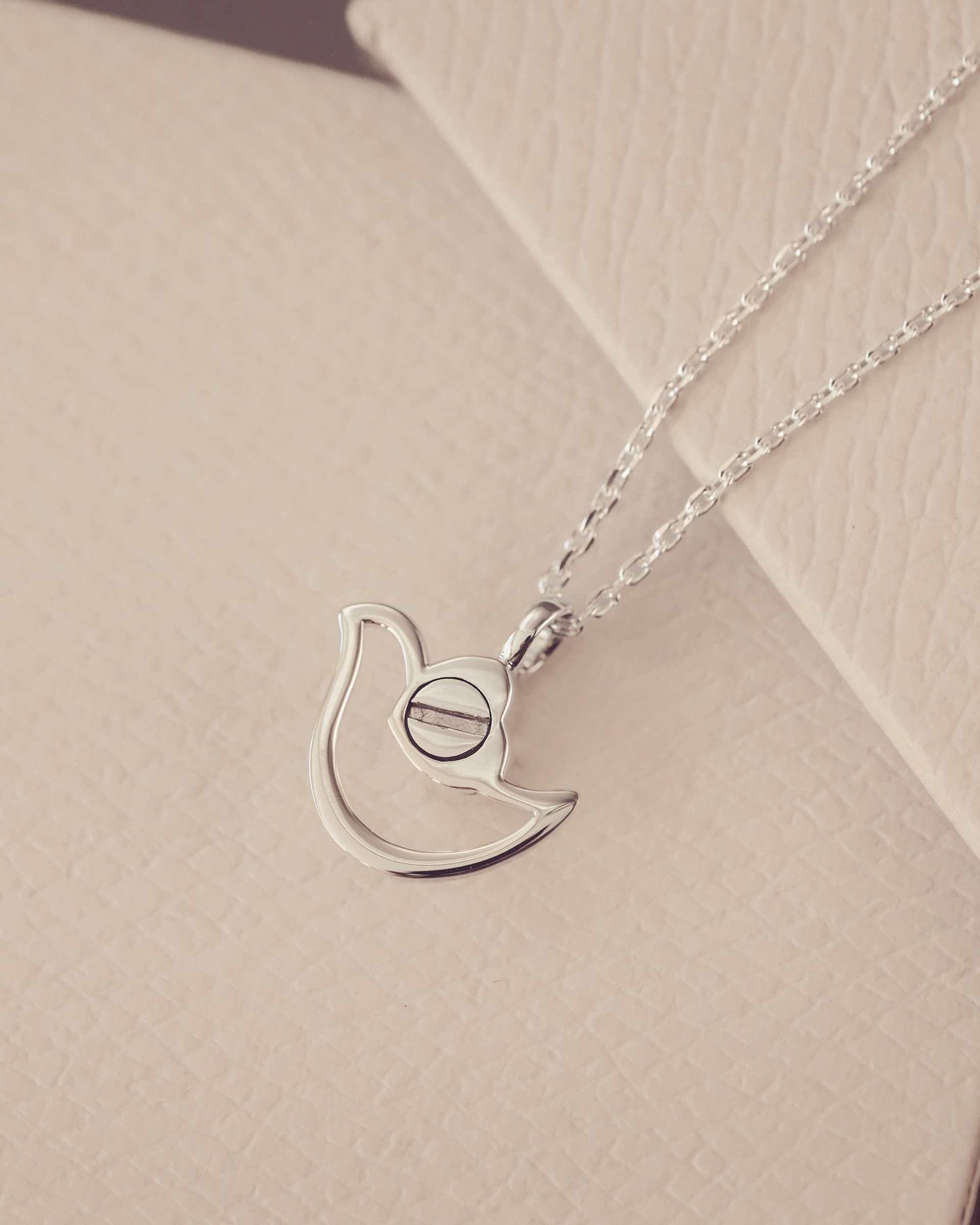 The back of a Silver urn necklace on a beige surface