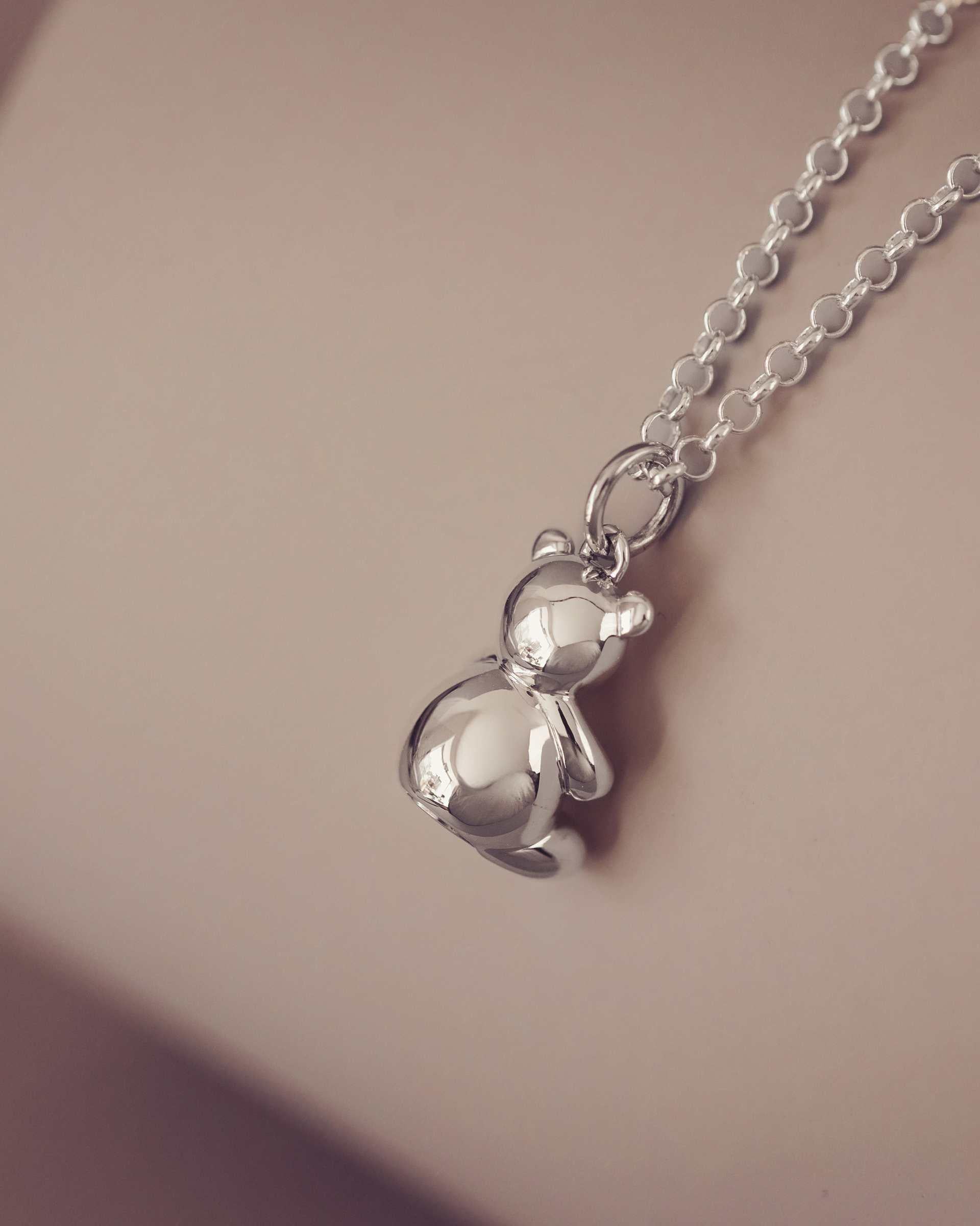 Silver Teddy bear pendant on a chain against a soft background