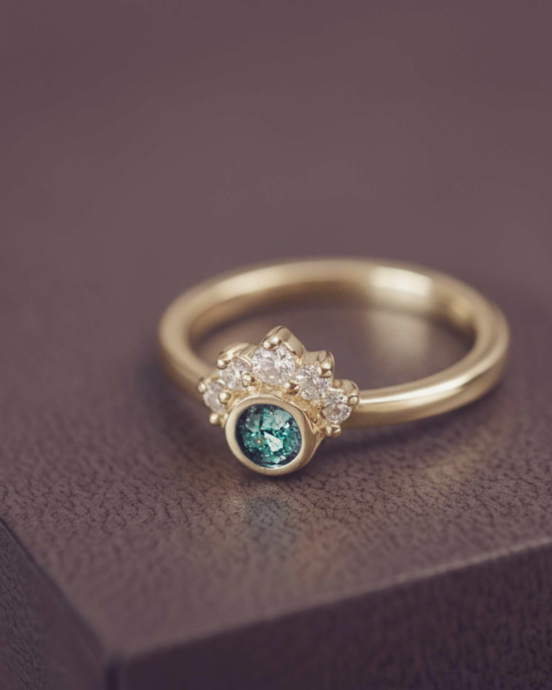 Gold cluster ring with a green centre and gemstone accents on a dark surface