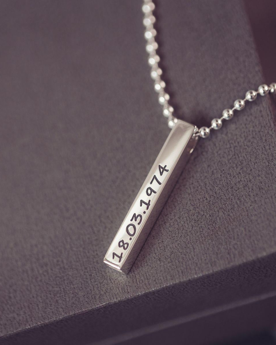 Silver necklace with a bar pendant displaying a date on a dark surface
