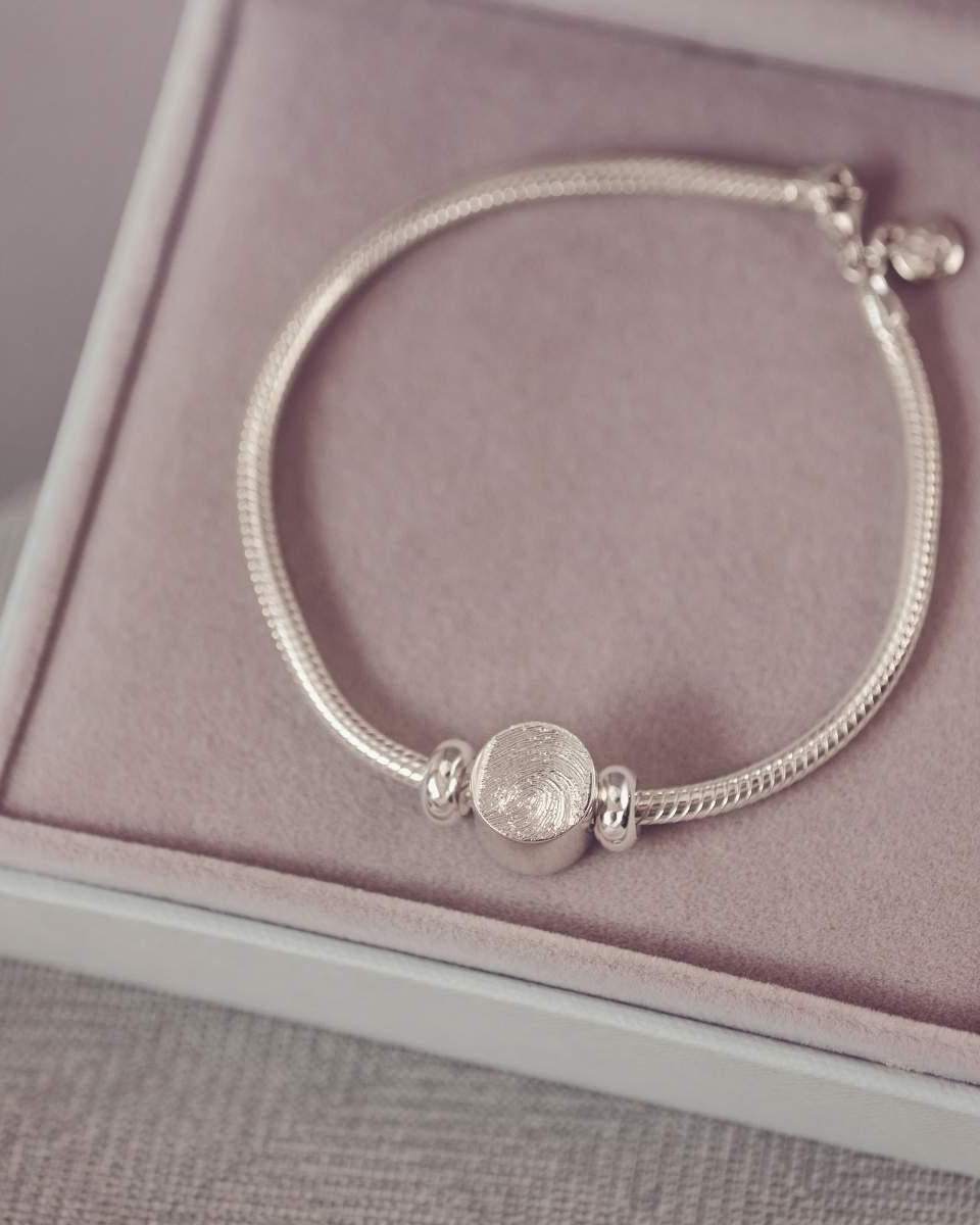 Silver bracelet with a round charm on a pink cushioned surface