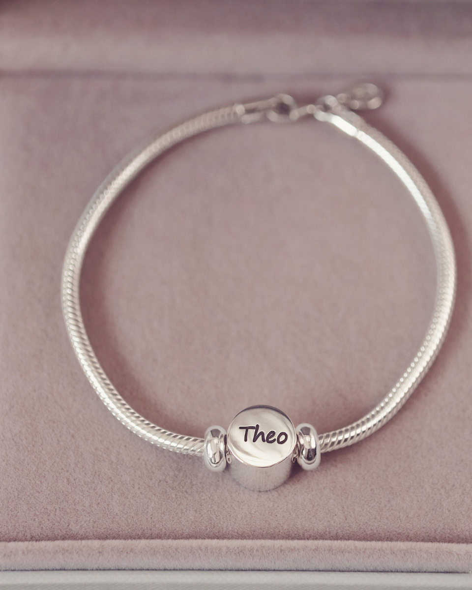 Silver bracelet with a round charm on a pink cushion