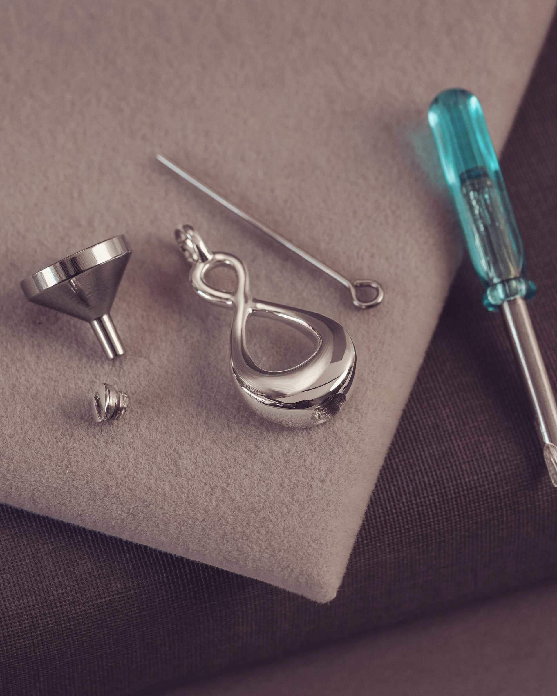 Silver pendant with a jewelery tools including a screwdriver on a textured surface