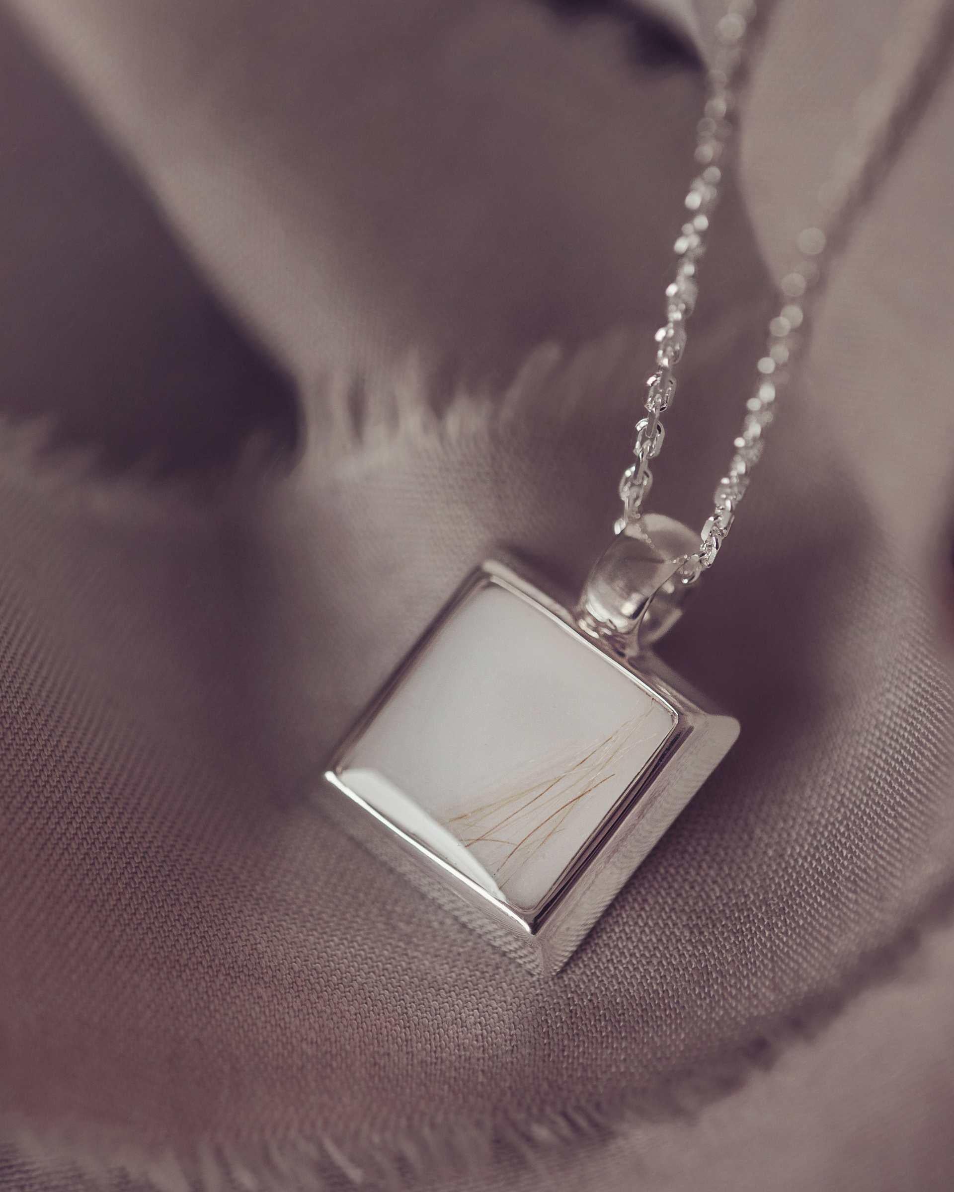 Silver necklace with a square pendant on a soft fabric background