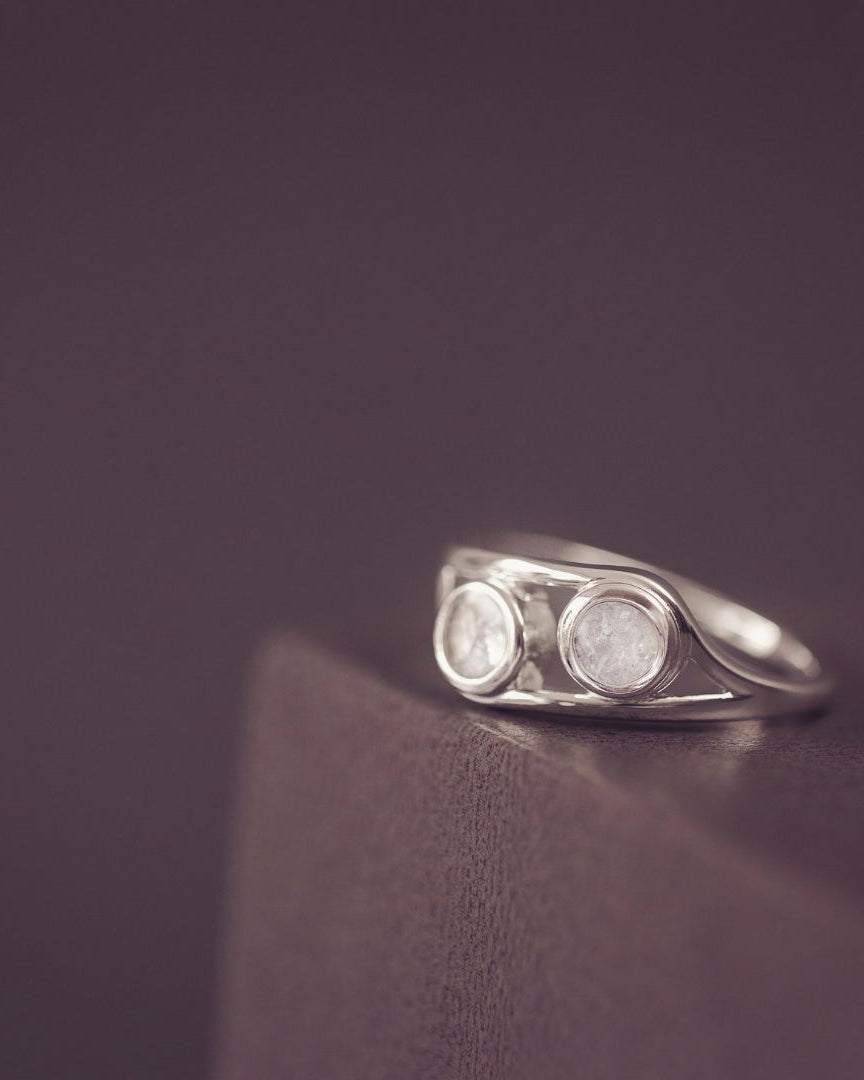 Silver ring with two circular stones on a dark purple background