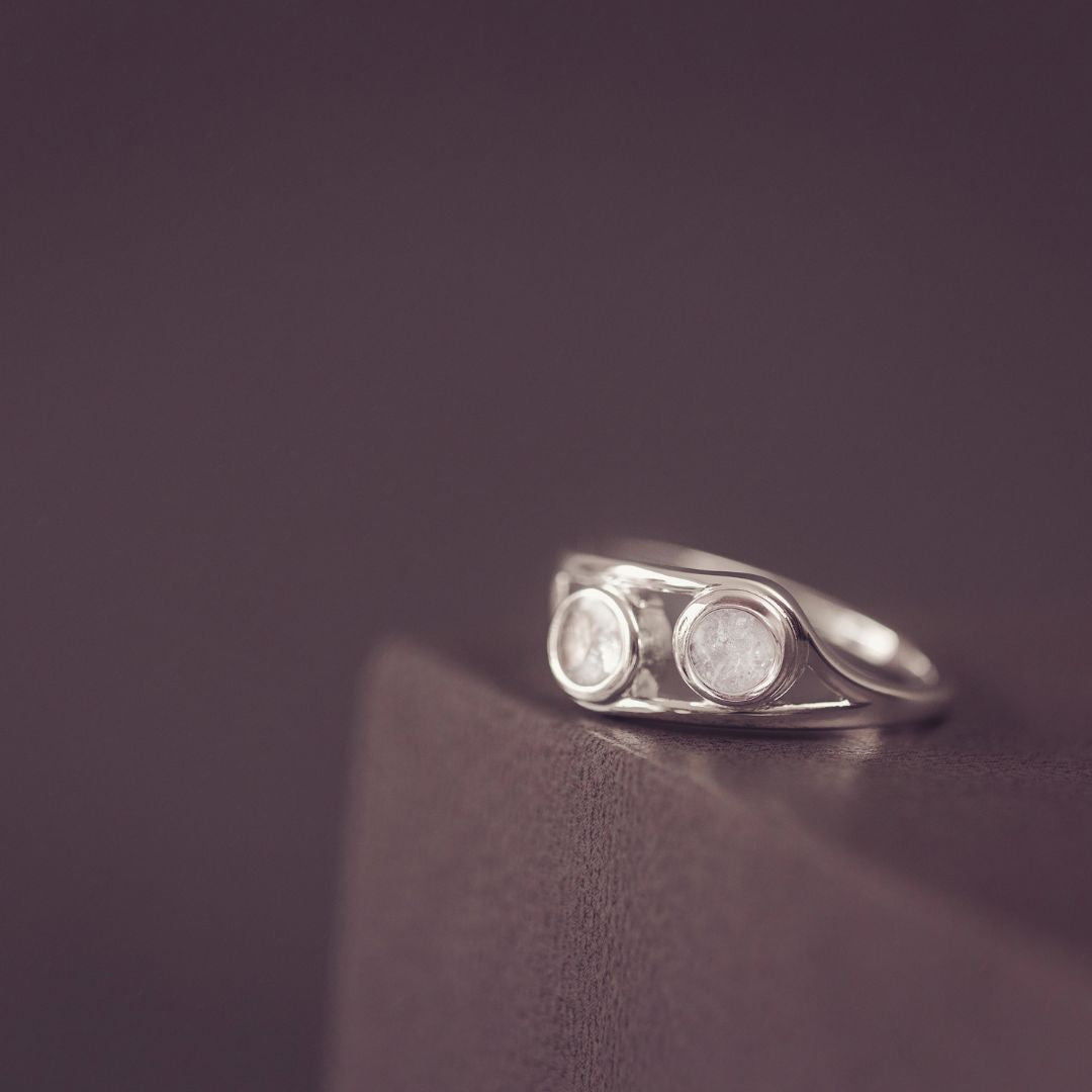 Silver ring with two circular stones on a dark purple background