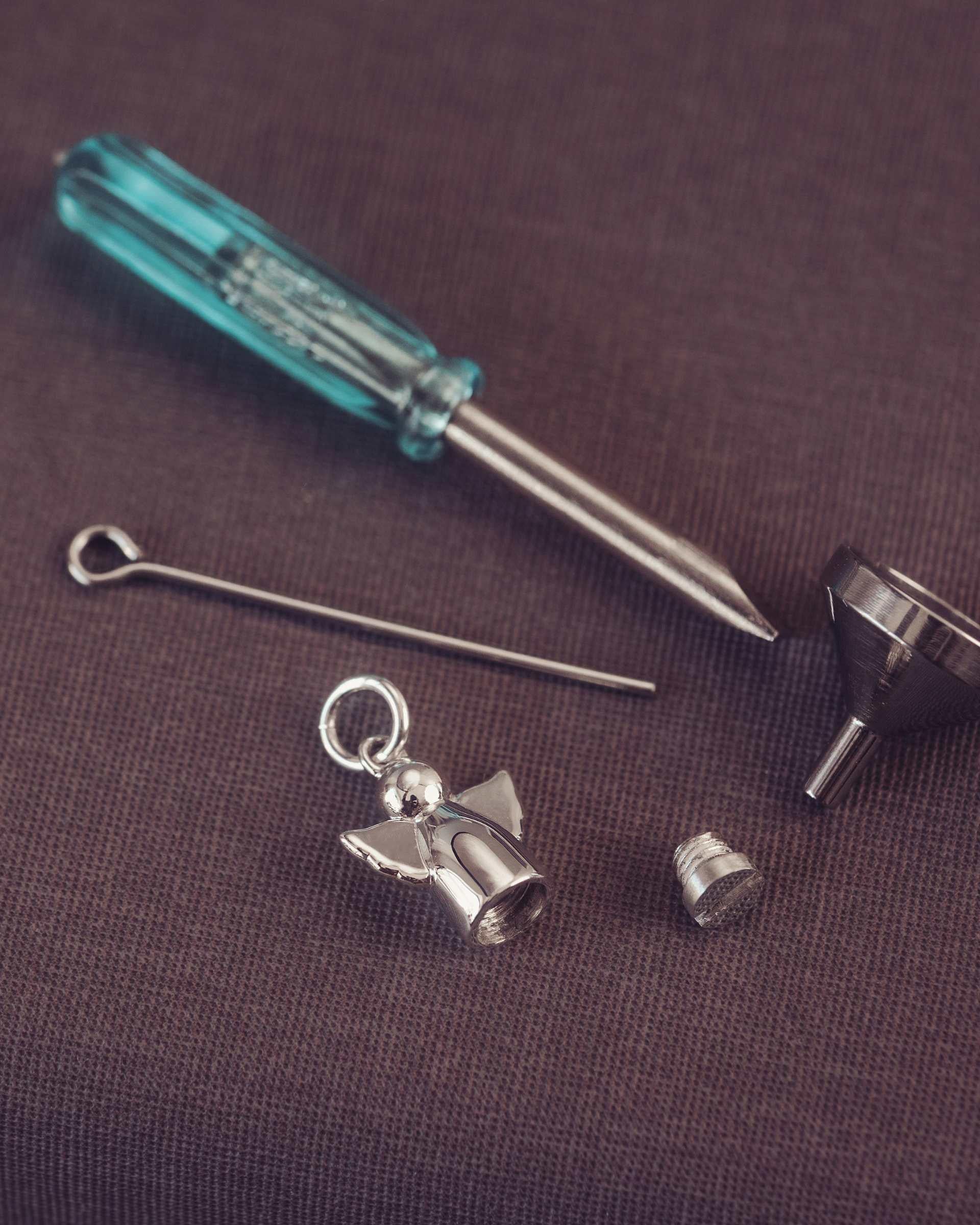 Set of jewellery tools including a screwdriver, needle, angel charm, and funnel on a brown background.