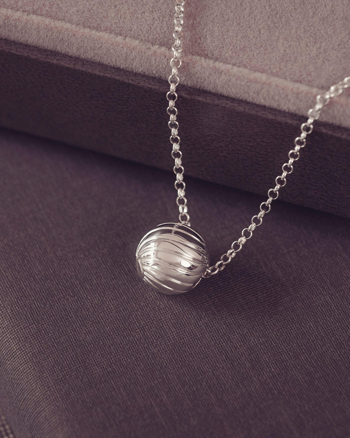 A silver beaded chain necklace with a wave spherical pendant, displayed on a dark textured fabric