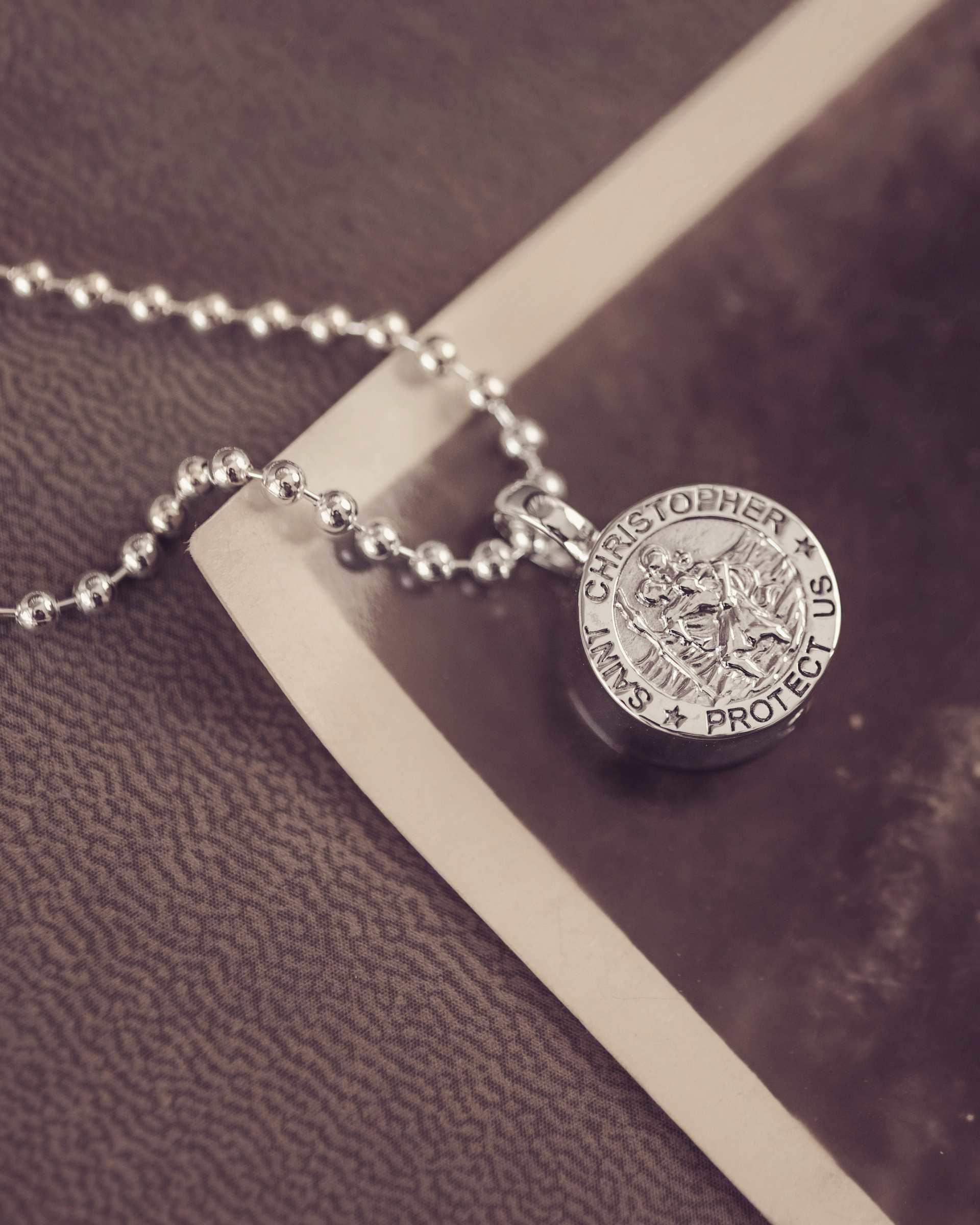 Silver necklace with a St Christopher pendant on a textured surface and vintage photograph
