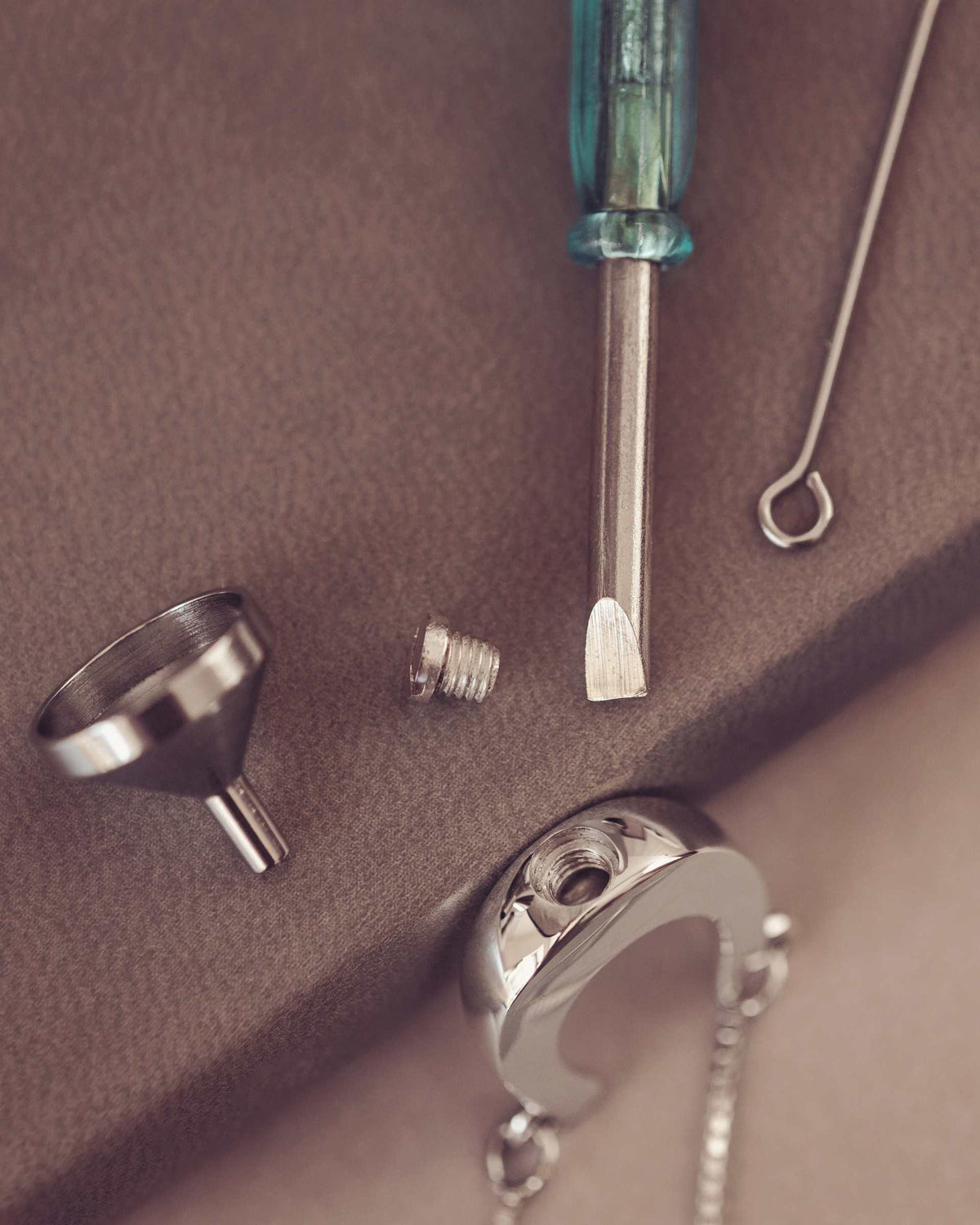 Jewelry-making tools including a funnel, screwdriver on a brown surface.