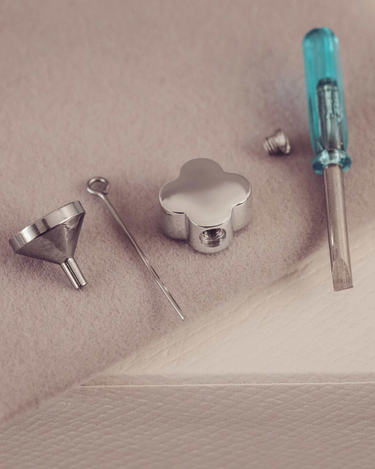 Set of jewellery tools including a funnel, screwdriver and pendant on beige surface.