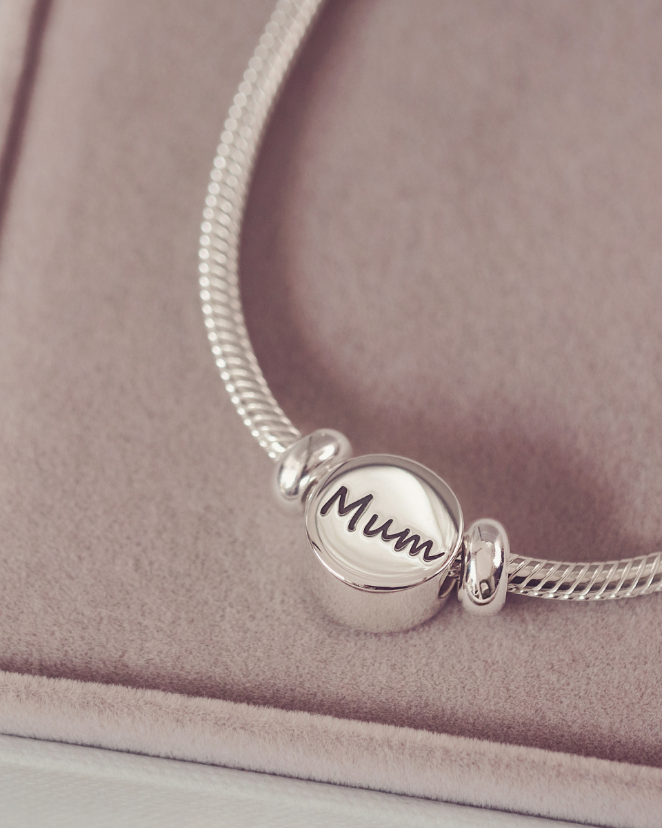 Silver bracelet with a 'Mum' charm on a soft pink background