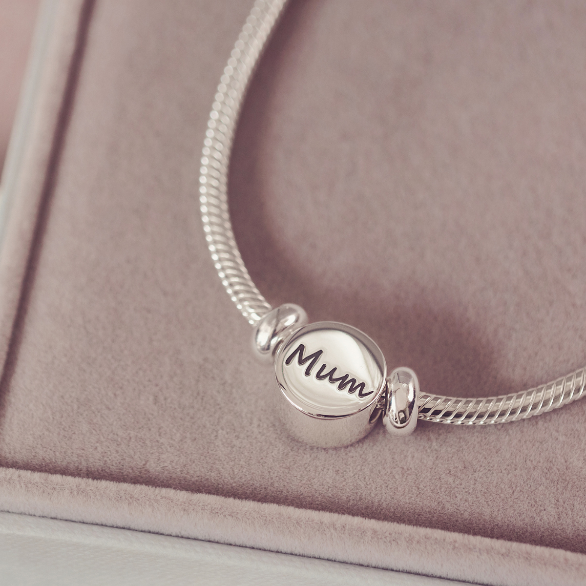 Silver bracelet with a 'Mum' charm on a soft pink background