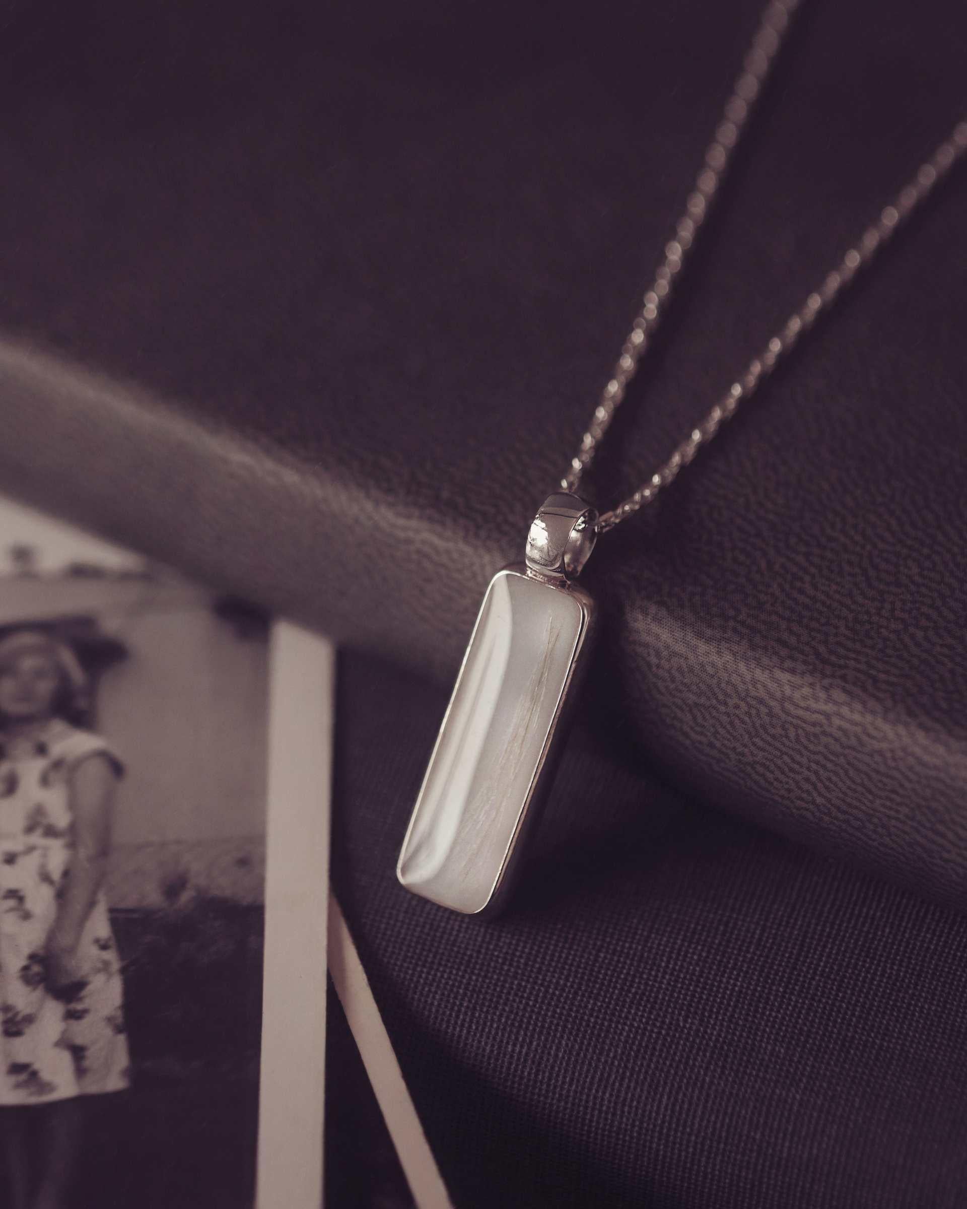 Silver pendant necklace on a dark fabric background with an old photograph of a woman in a floral dress.