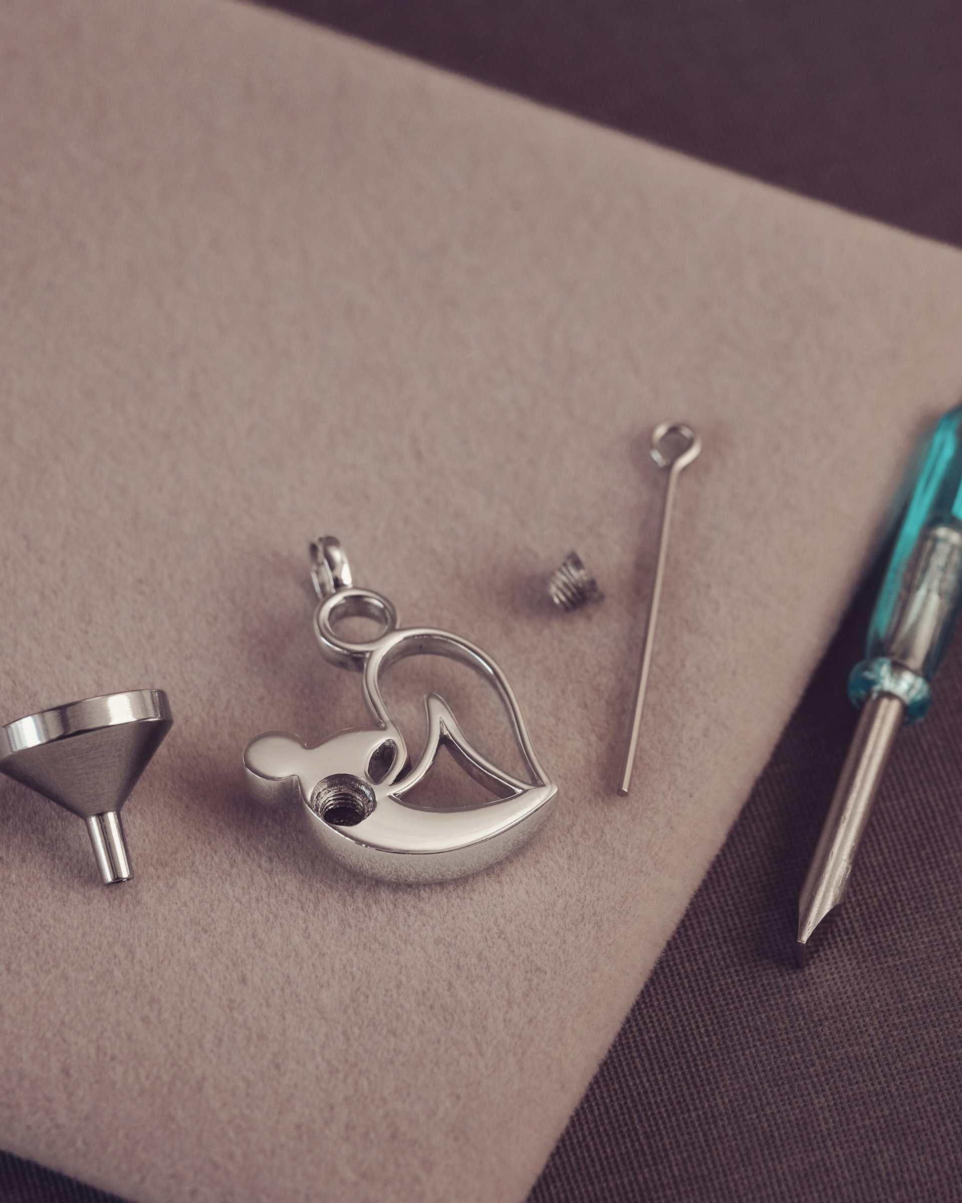 Silver pendant, funnel and screwdriver on a brown surface