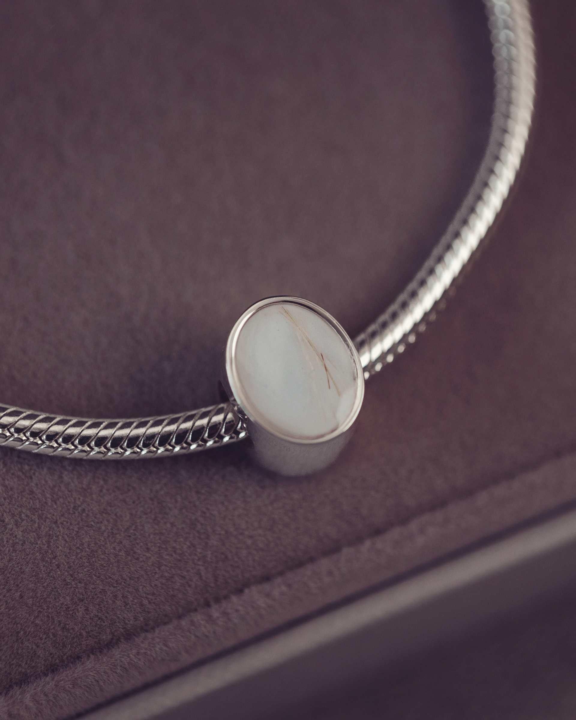 Silver bracelet with an oval charm on a dark surface