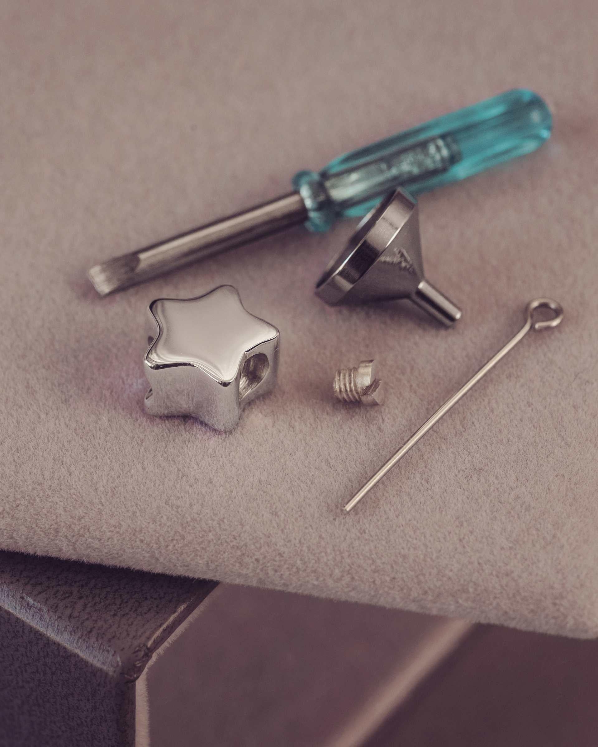 Set of jewelry-making tools including a star-shaped component, screwdriver, and needle on a textured surface.