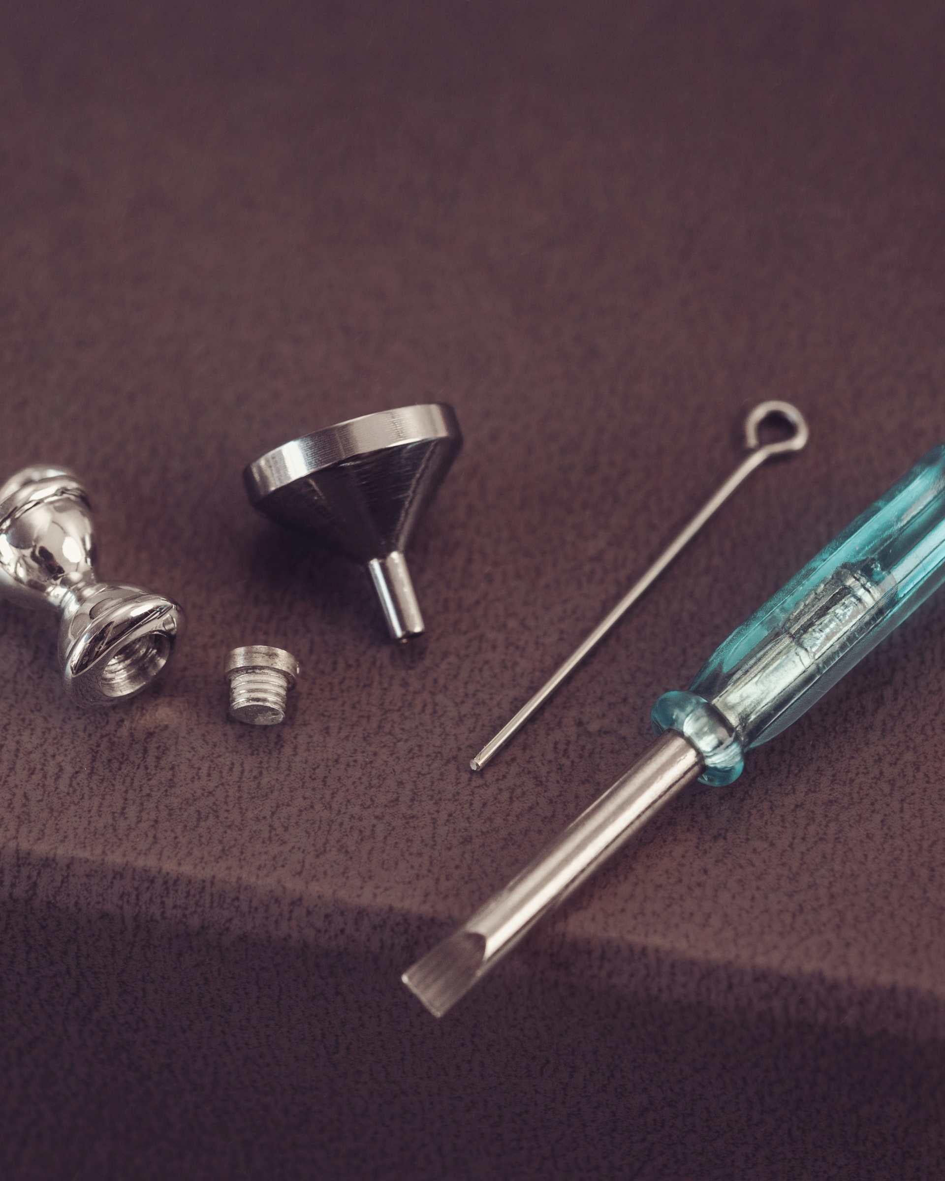 Set of metal tools including a screwdriver, funnel, and hourglass pendant on a brown surface.