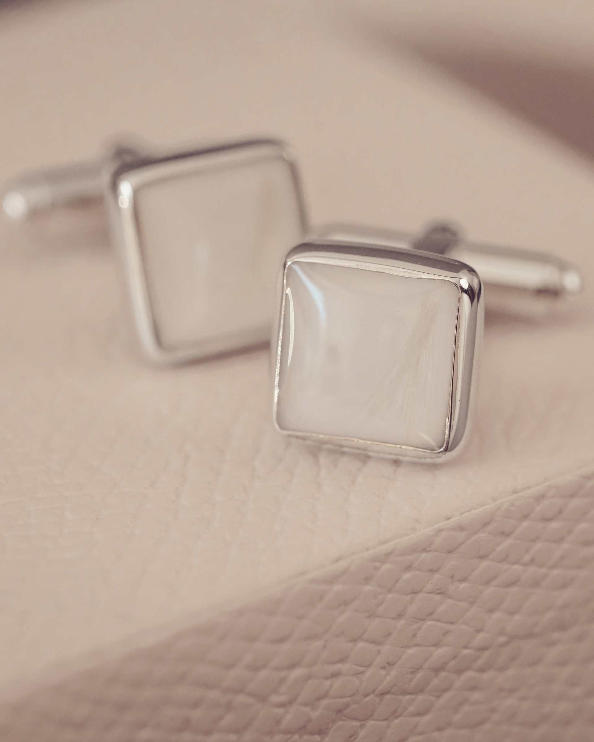 Silver square cufflinks on a textured beige surface