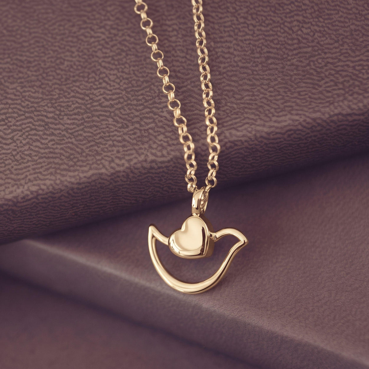 A gold necklace with a bird-shaped pendant and a small heart detail, displayed on a textured brown surface.