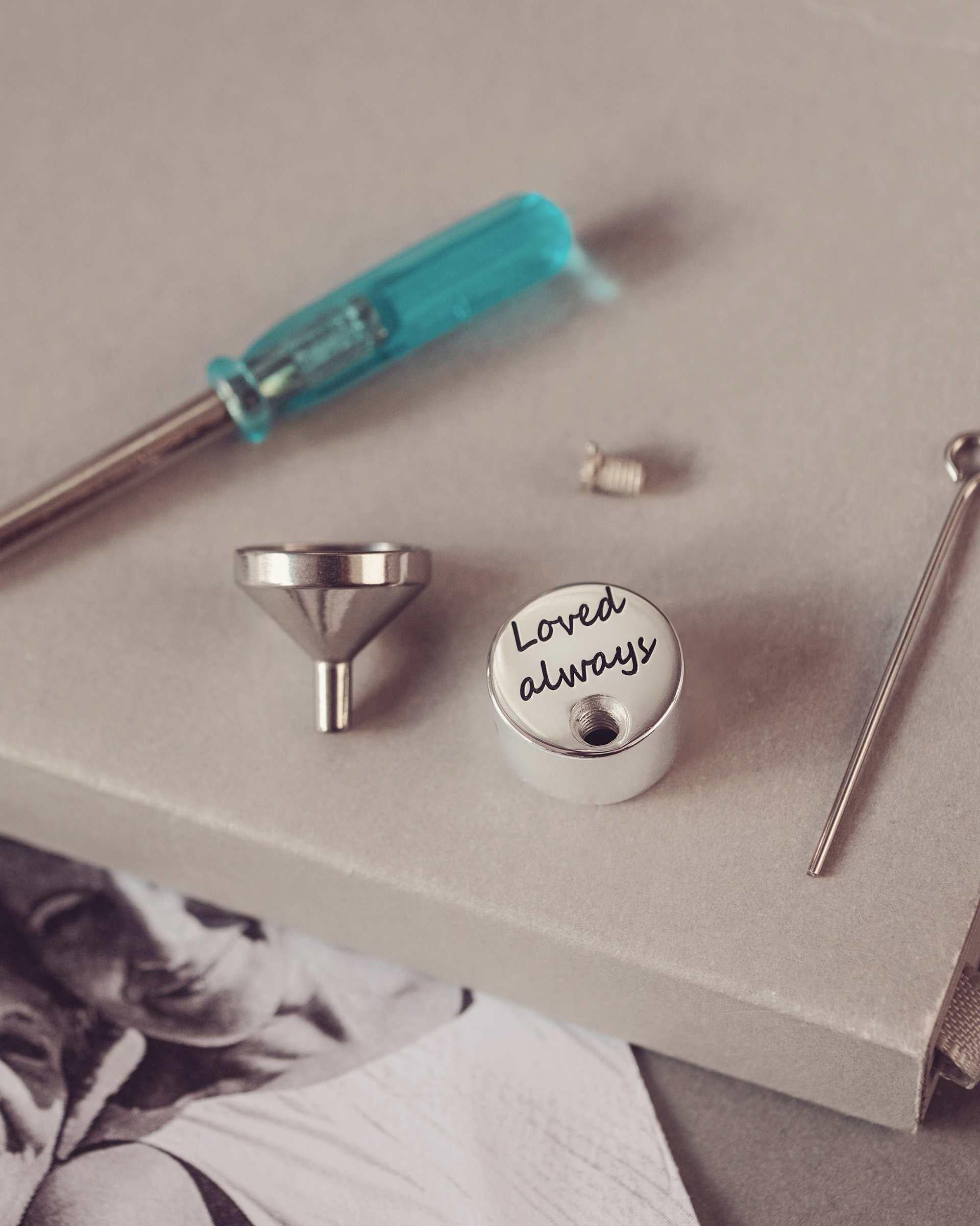 Set of small tools including a screwdriver, funnel and round charm on a textured surface.