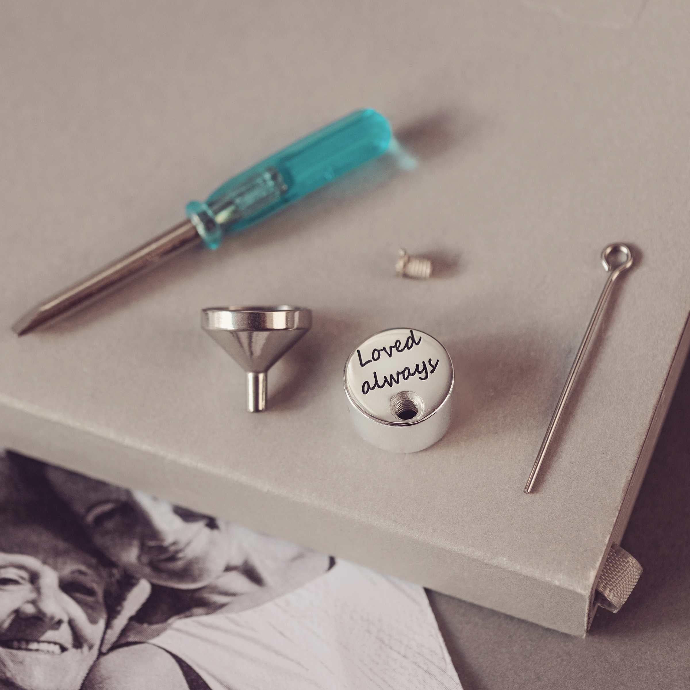 Set of small tools including a screwdriver, funnel and round charm on a textured surface.