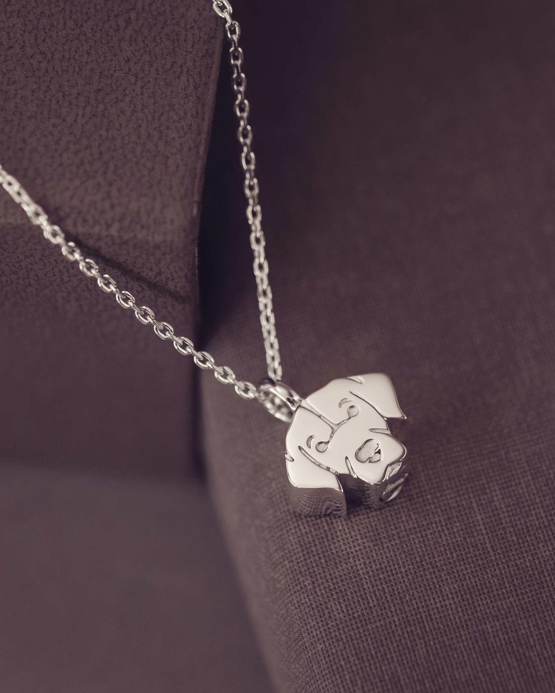 Silver Labrador dog-shaped pendant on a chain against a dark fabric background
