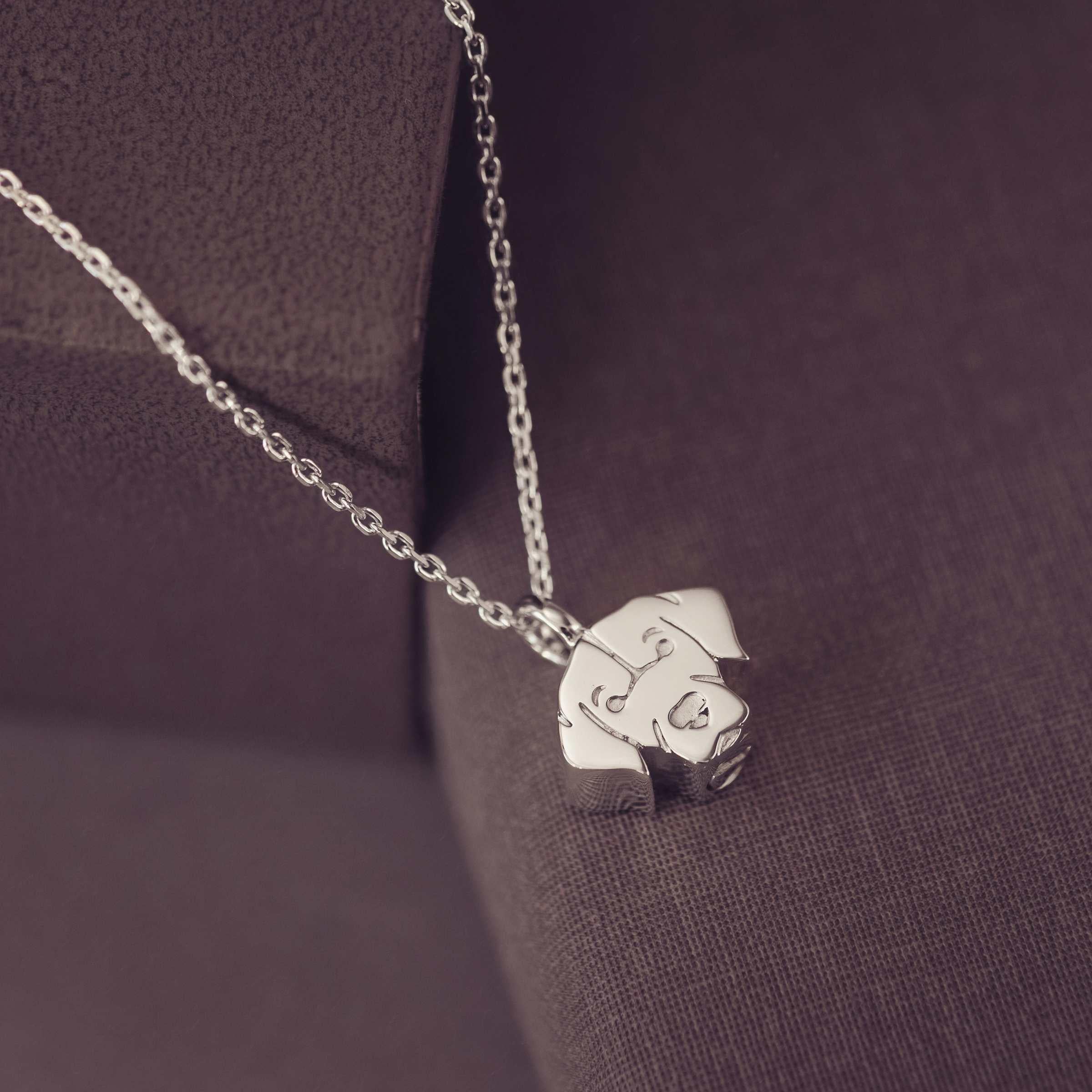 Silver Labrador dog-shaped pendant on a chain against a dark fabric background