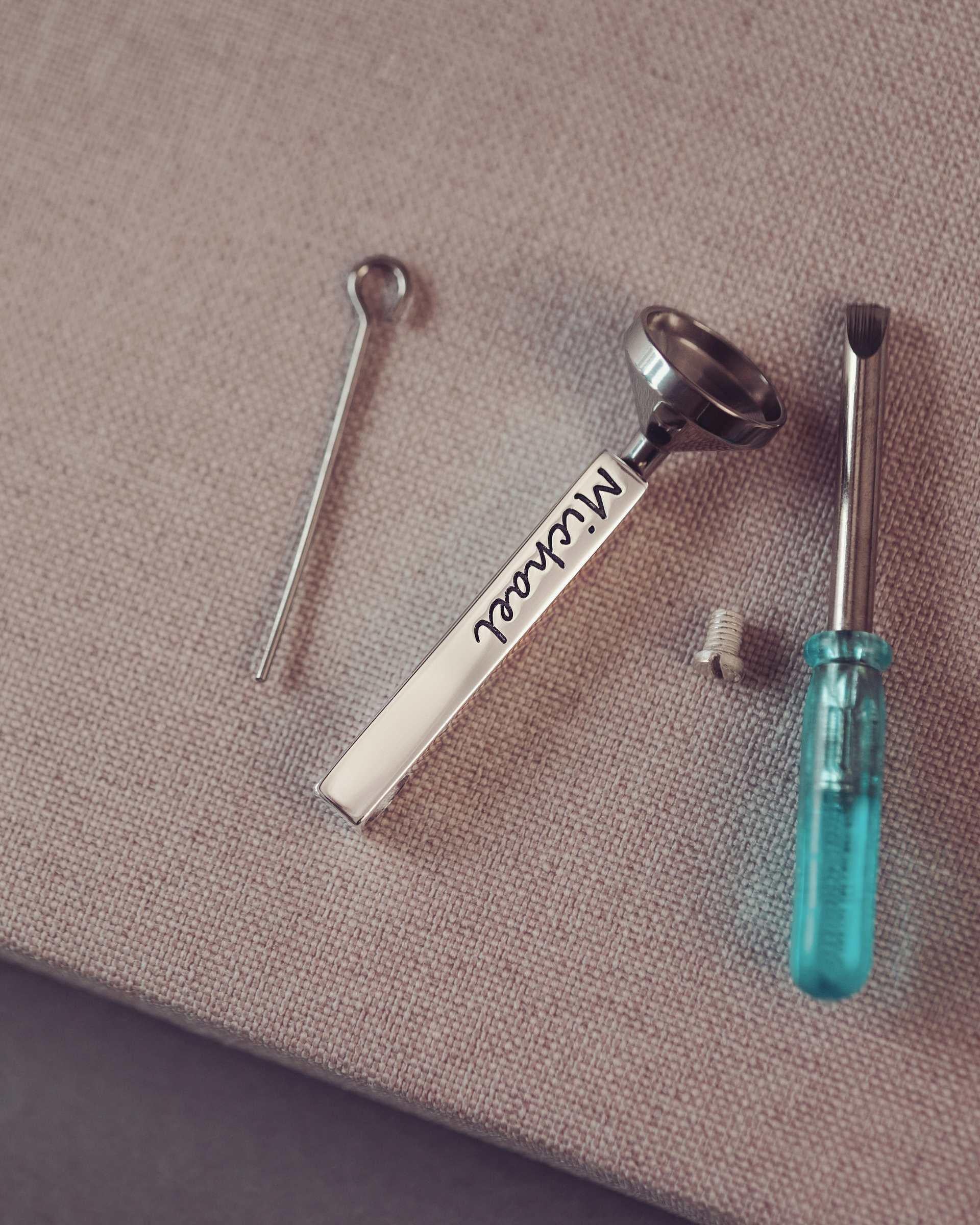 Set of small tools including a screwdriver, funnel and bar pendant on a textured surface.