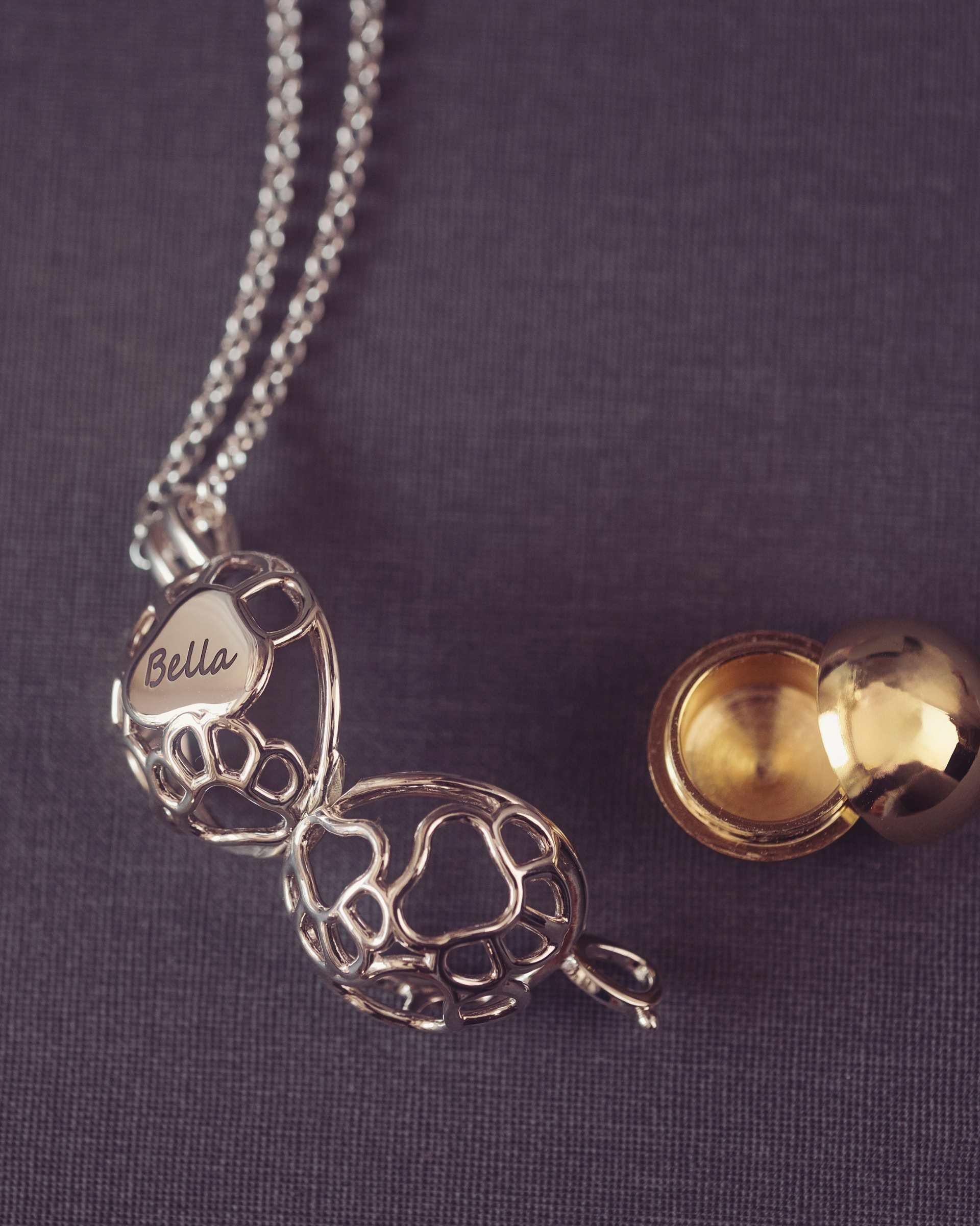 Silver necklace with a paw shaped pendant and yellow locket on a purple fabric background
