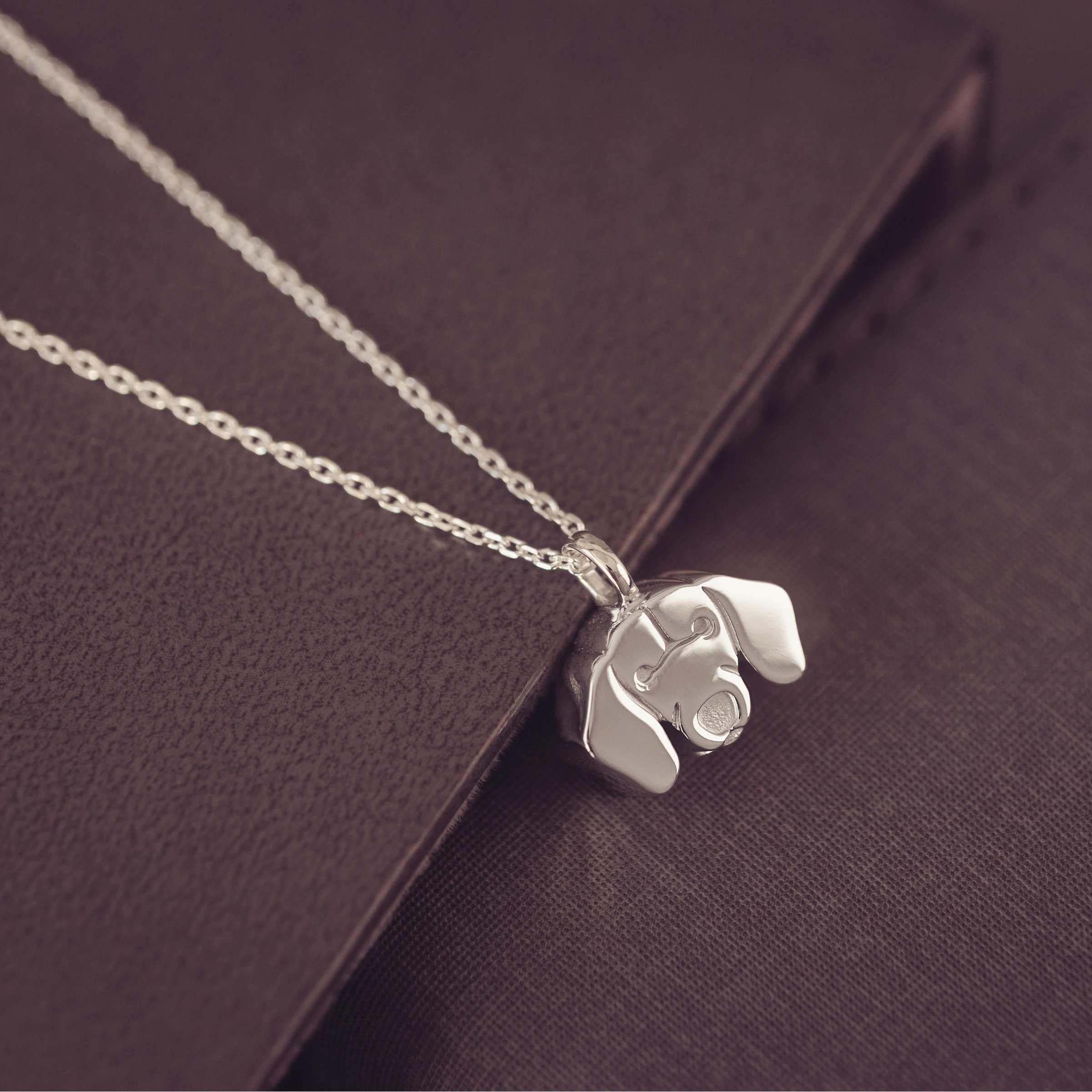 Silver dog-shaped pendant on a chain against a dark brown background