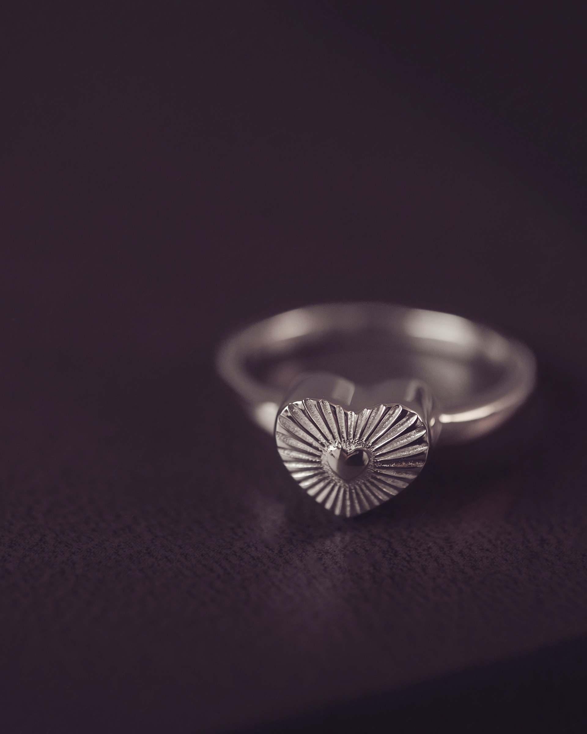 Silver ring with a textured heart-shaped design on a dark background