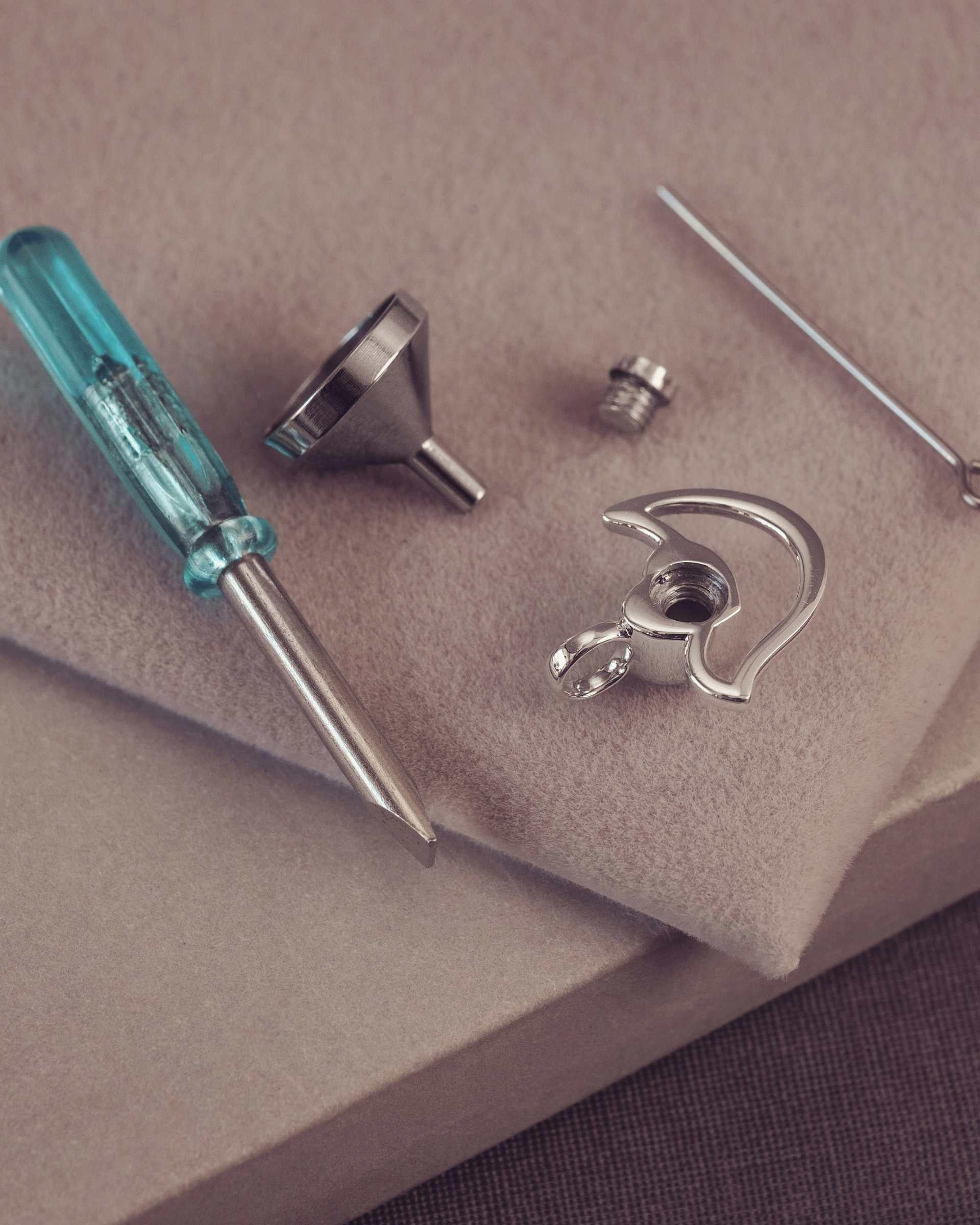 Jewellery tools including a screwdriver and metal components on a beige surface.