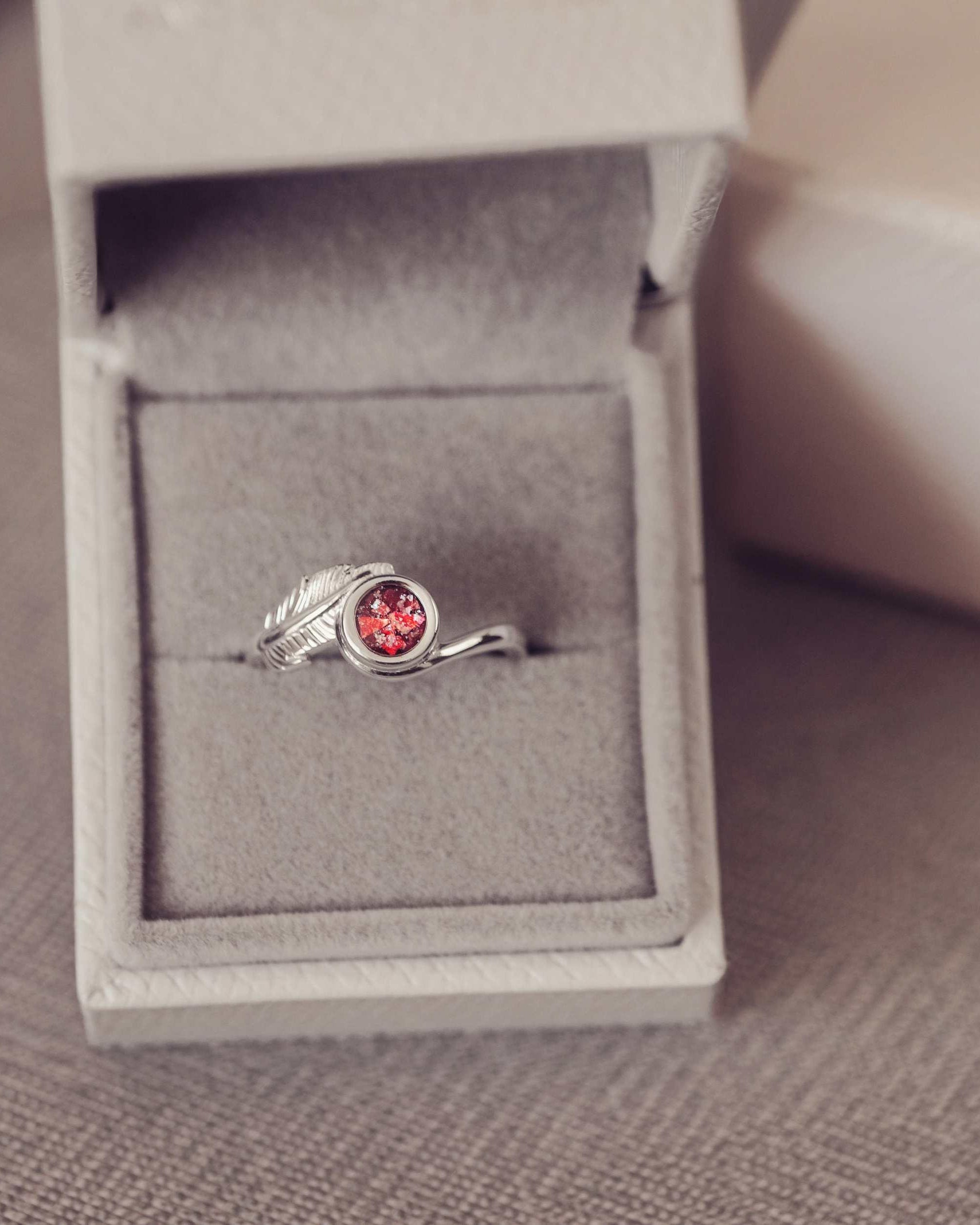 A silver red ash filled feather ring in a jewellery box