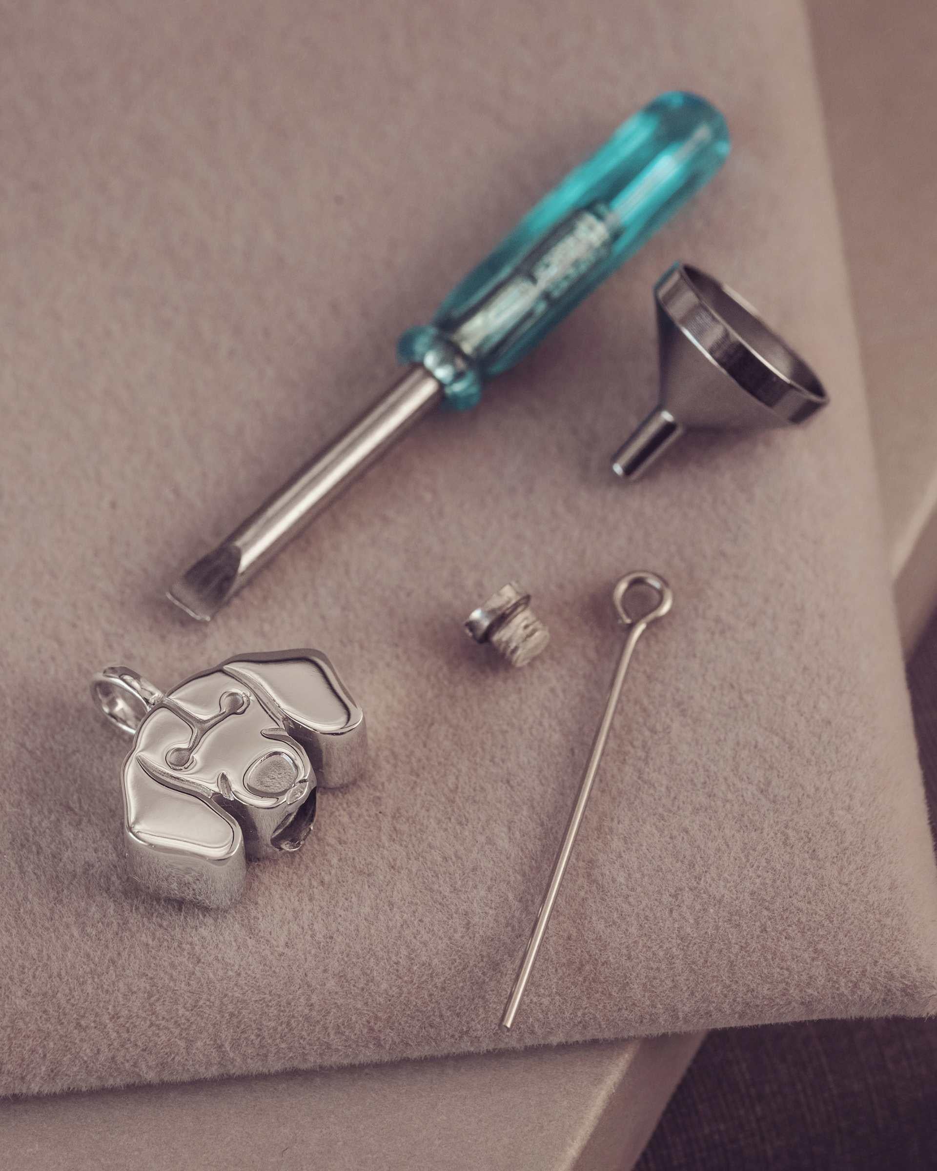 Jewelry-making tools including a screwdriver, funnel, and small components on a neutral surface.