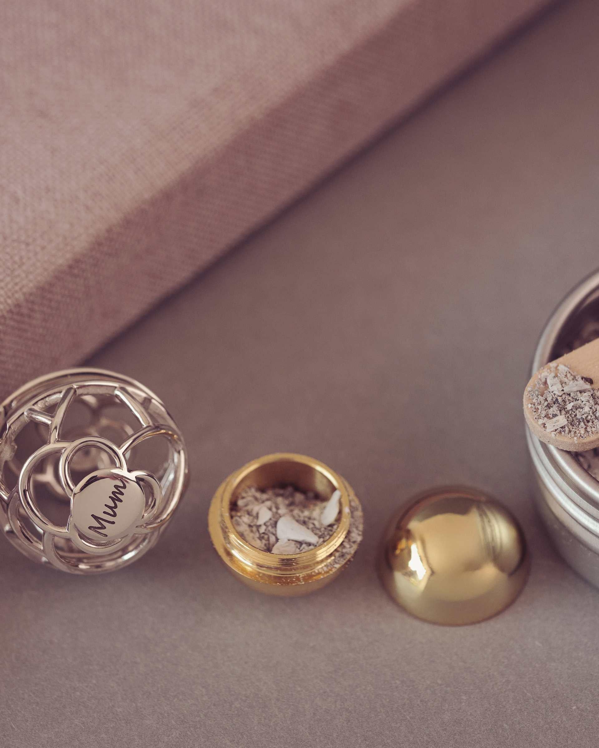 Silver necklace with a locket, gold container of ashes on a neutral background