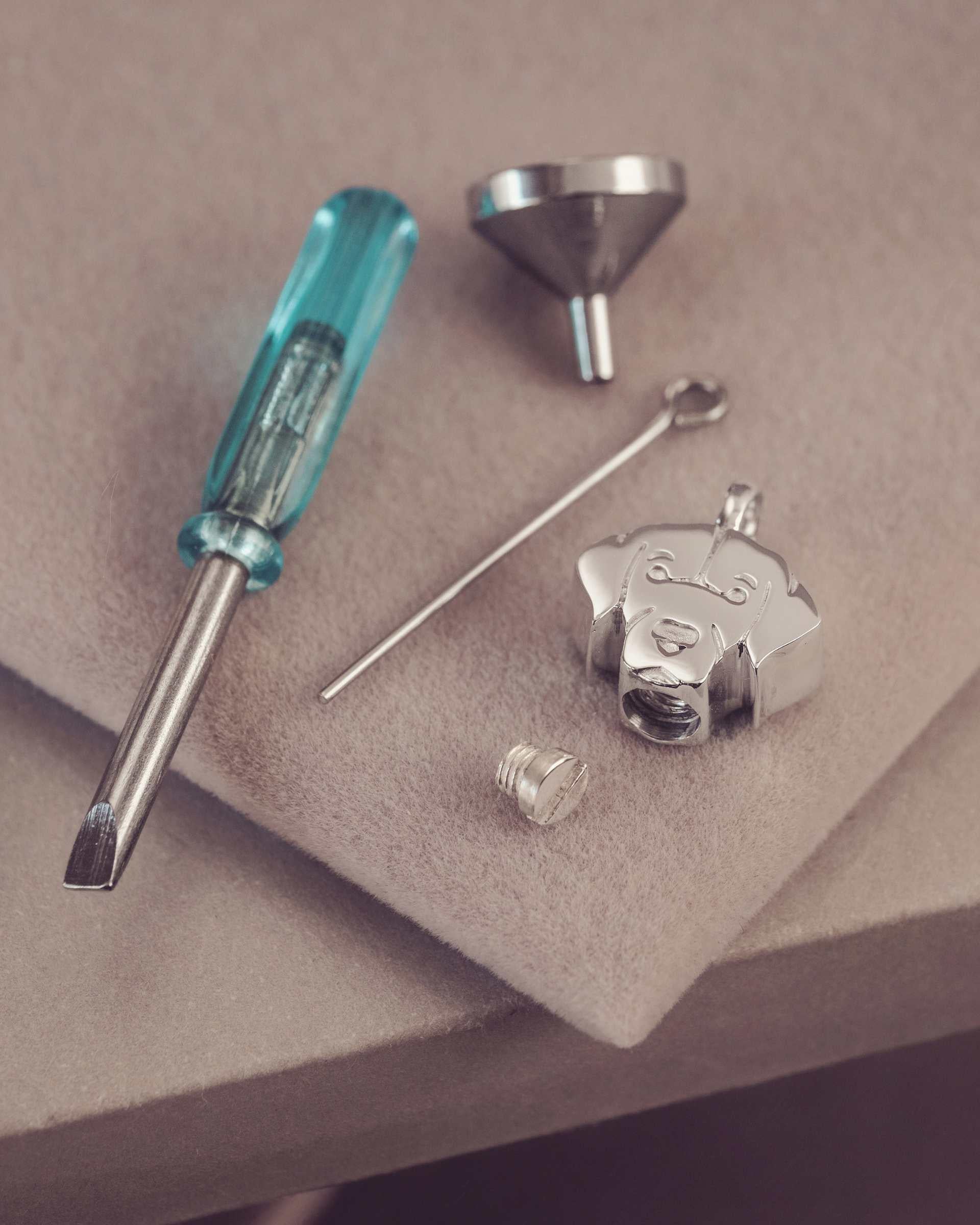 Jewelry-making tools including a screwdriver, funnel, and metal components on a beige surface.