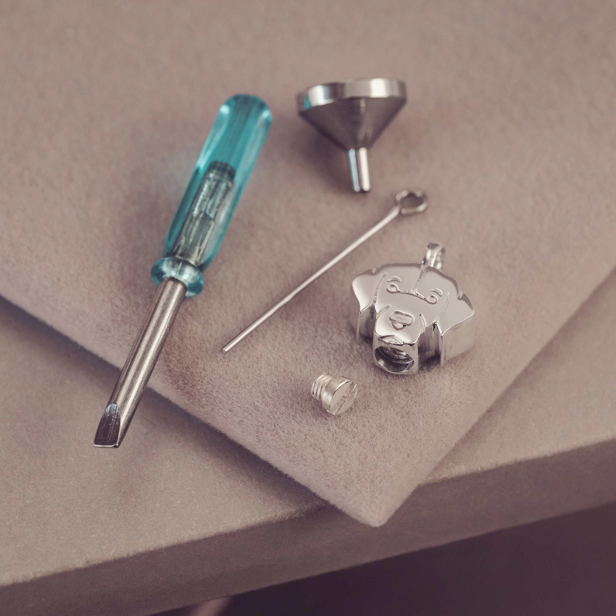 Jewelry-making tools including a screwdriver, funnel, and metal components on a beige surface.