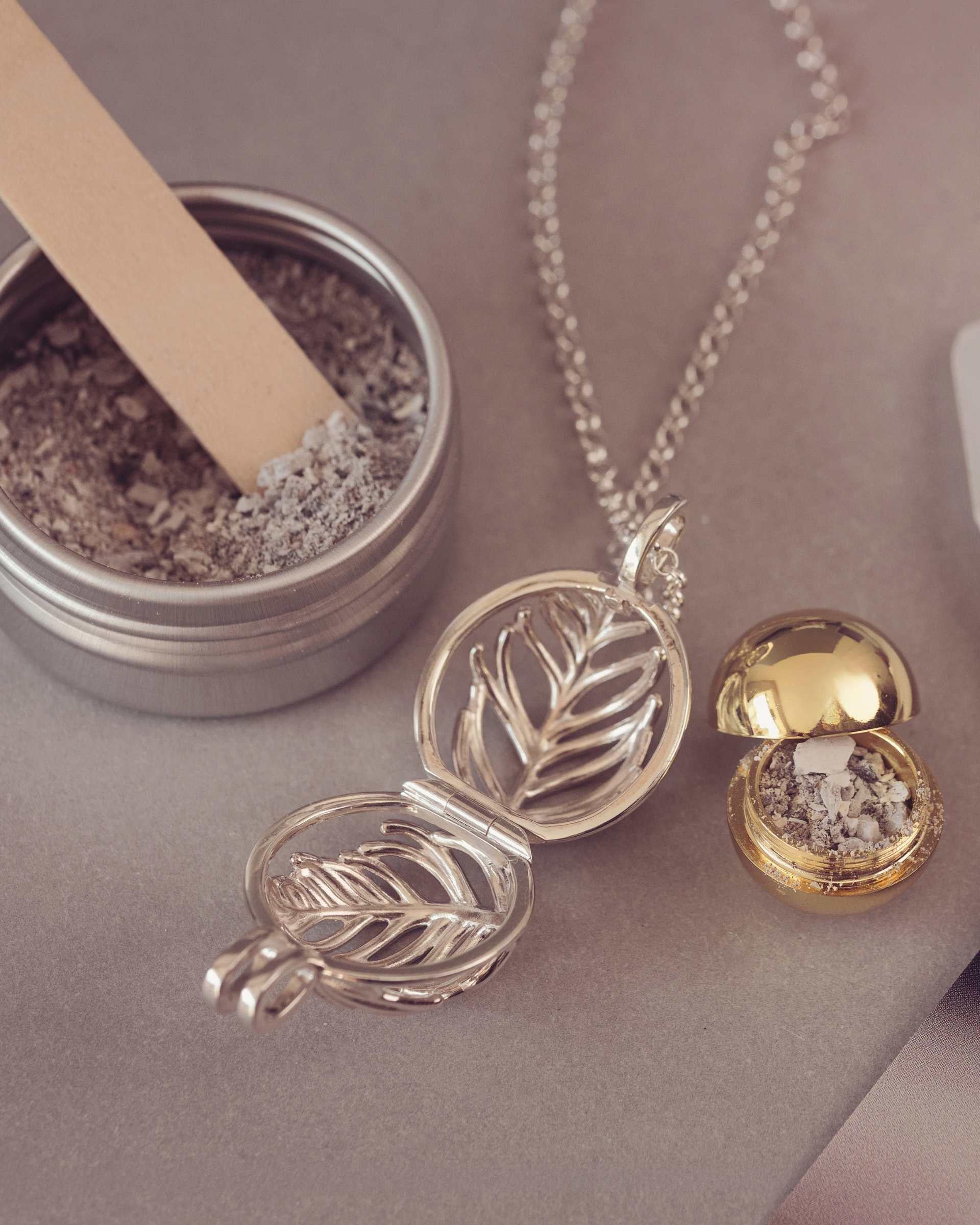 Silver and gold necklace with a small container of ash on a neutral background