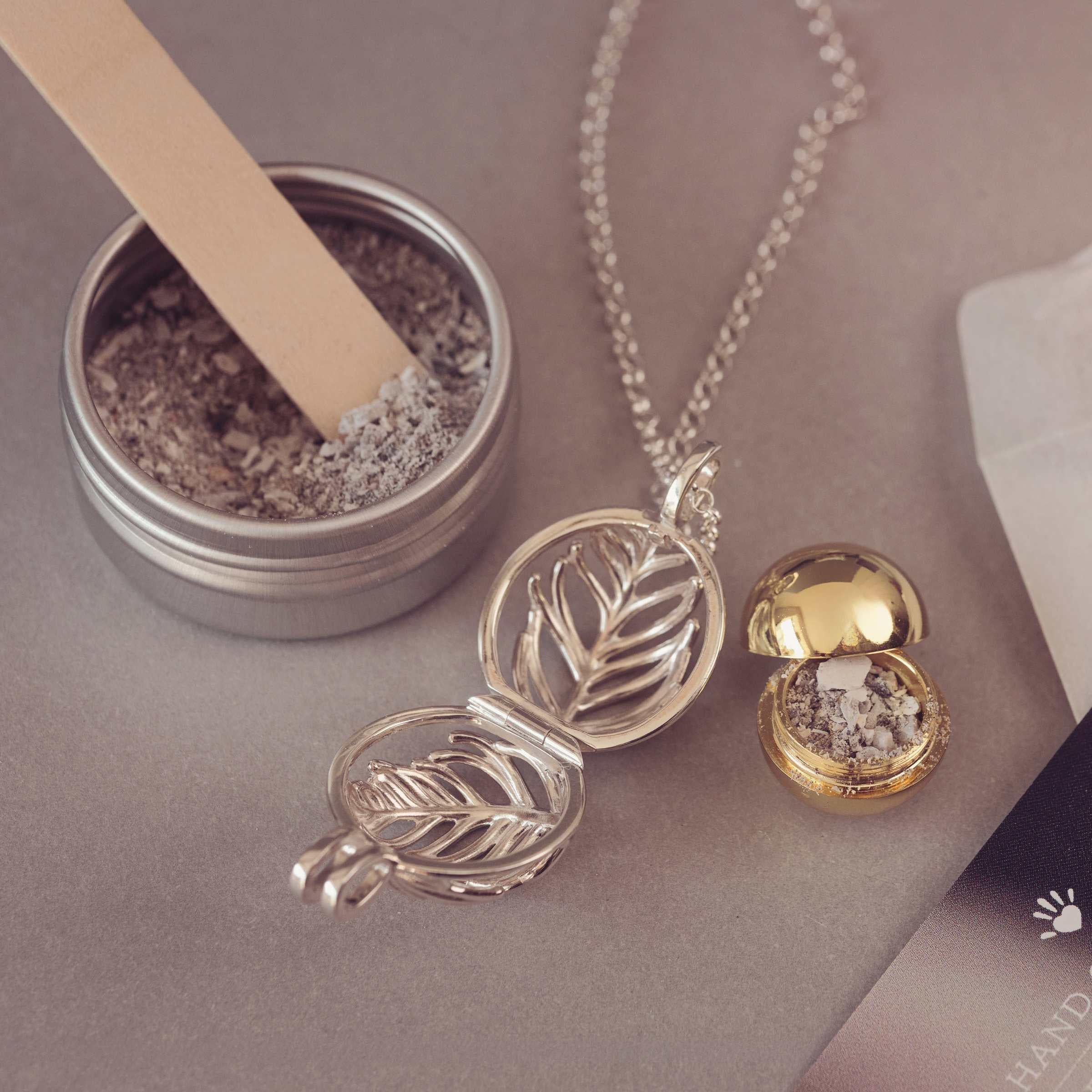Silver and gold necklace with a small container of ash on a neutral background