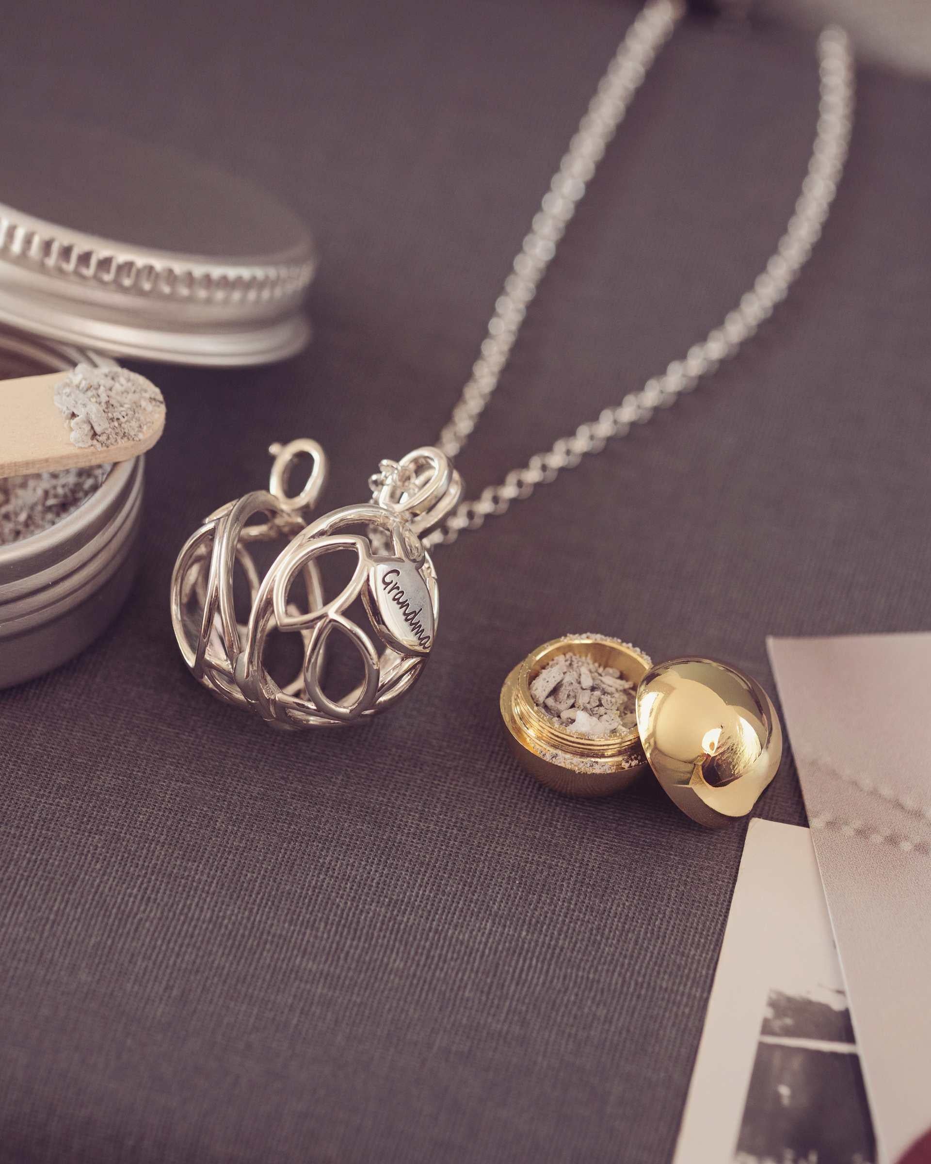 Silver and gold necklaces on a textured surface with small containers and photos.