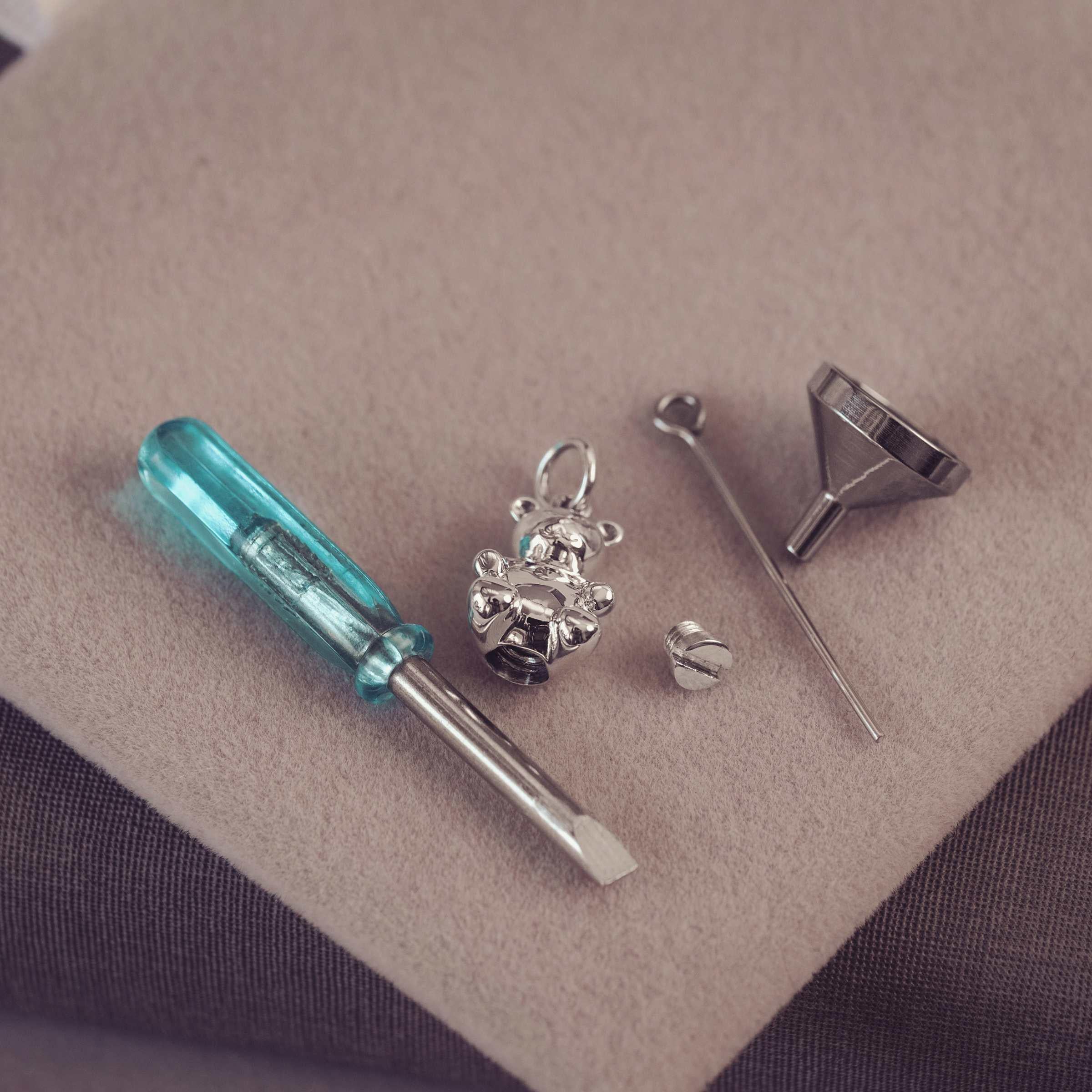 Jewelry-making tools including a screwdriver, funnel, and metal components on a beige surface.