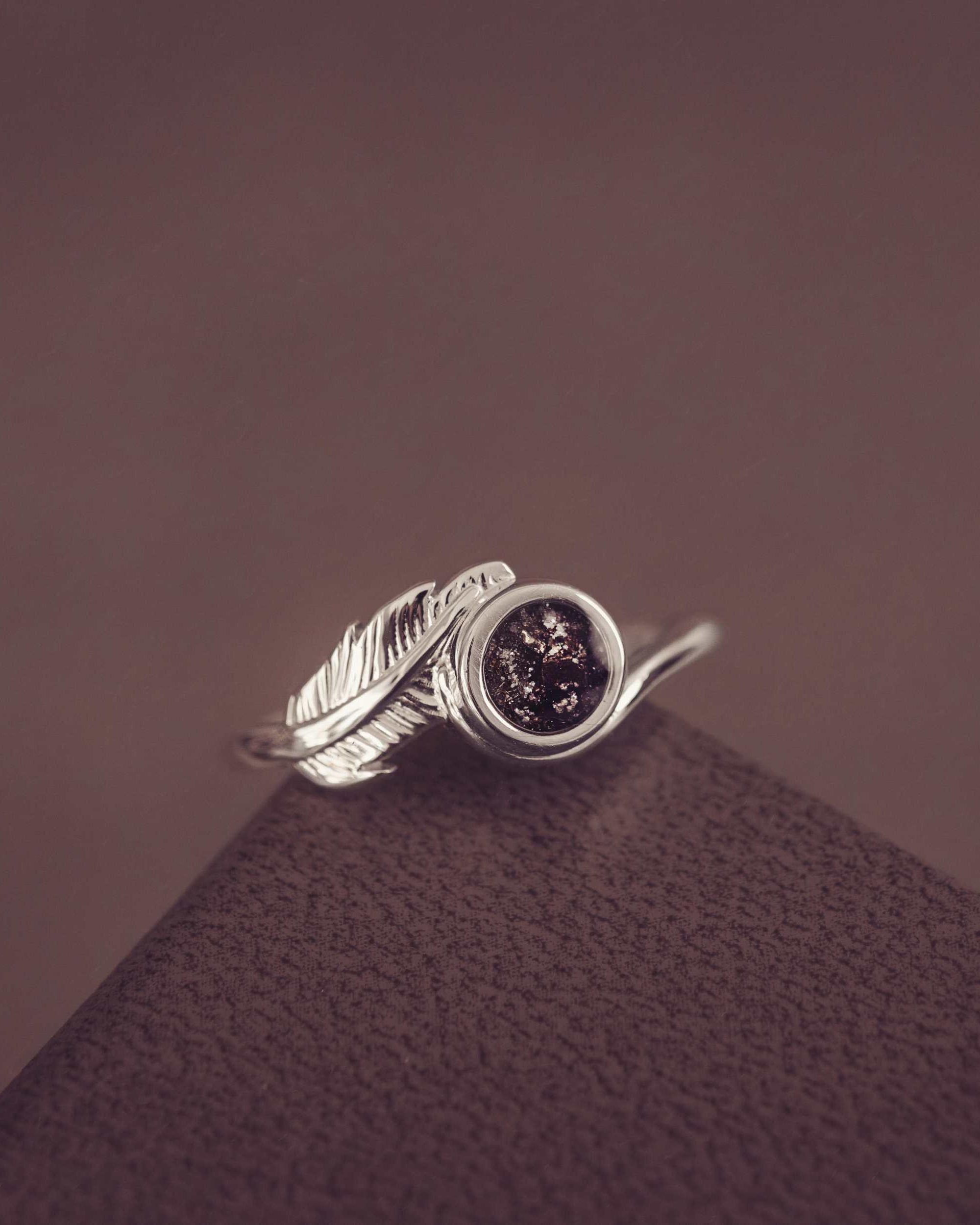 A silver black ash filled feather ring on dark textured background