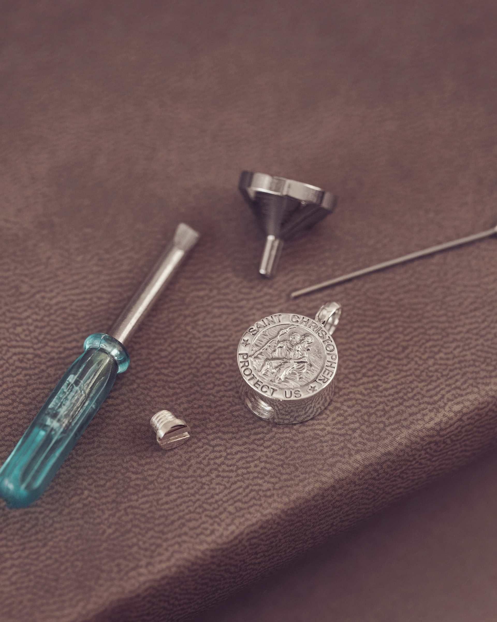 Silver pendant on a leather surface, surrounded by tools like a screwdriver and funnel.