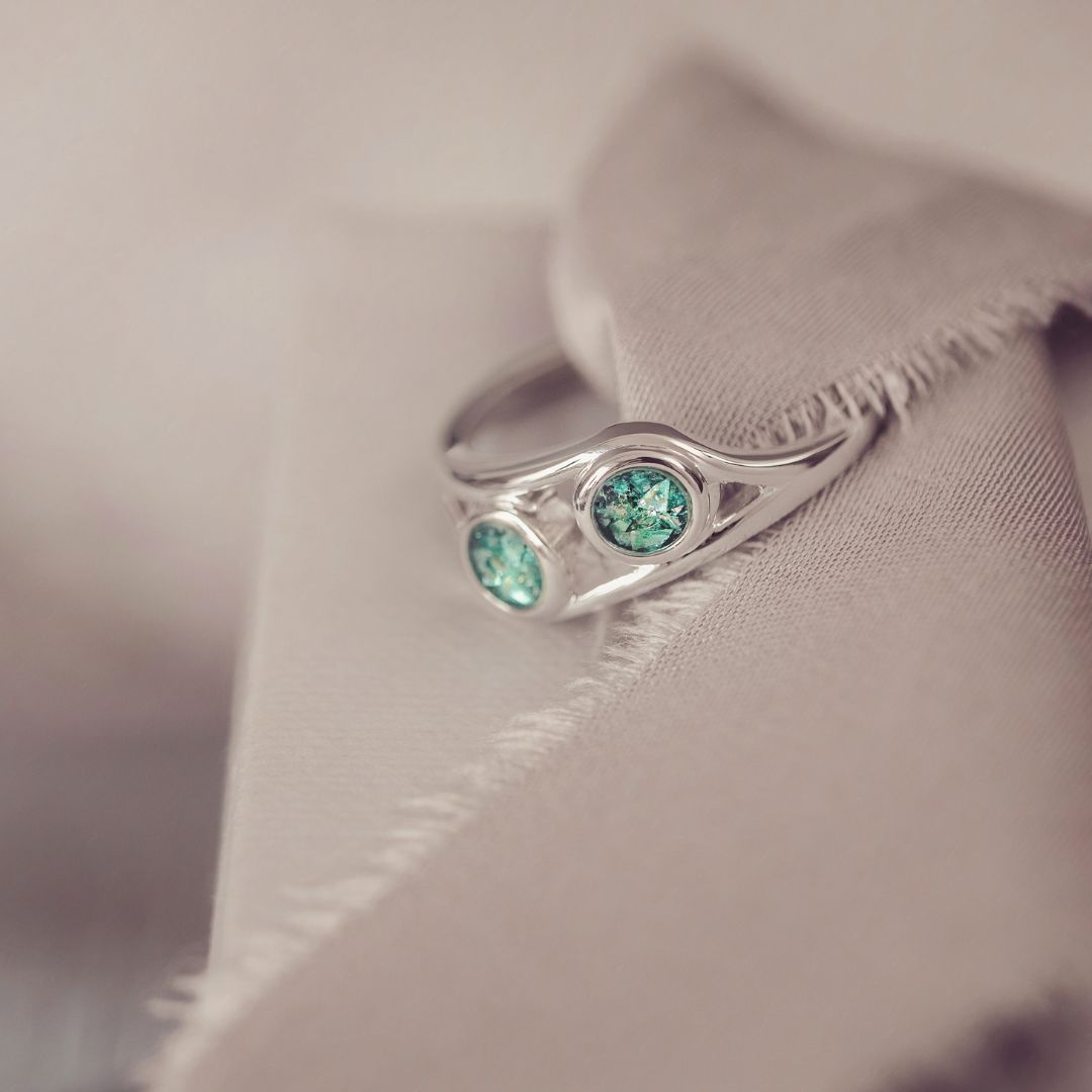 Silver ring with green gemstones on a soft fabric background
