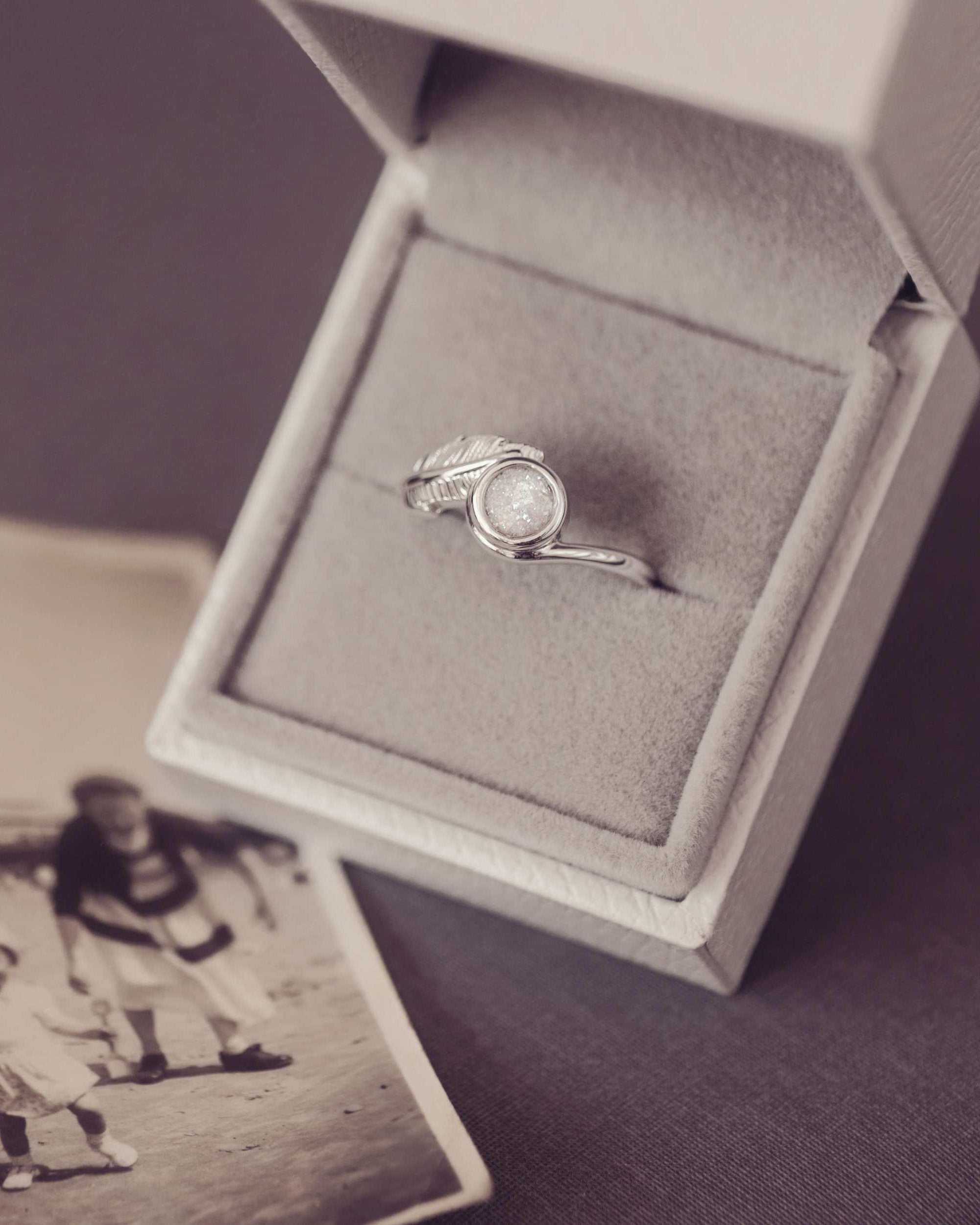 A silver ash filled feather ring in a jewellery box next to a black and white photograph